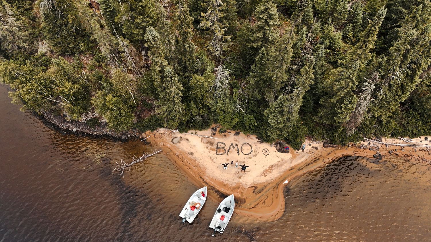 Aerial panorama of a shoreline with boats docked near a sandy beach surrounded by forest.