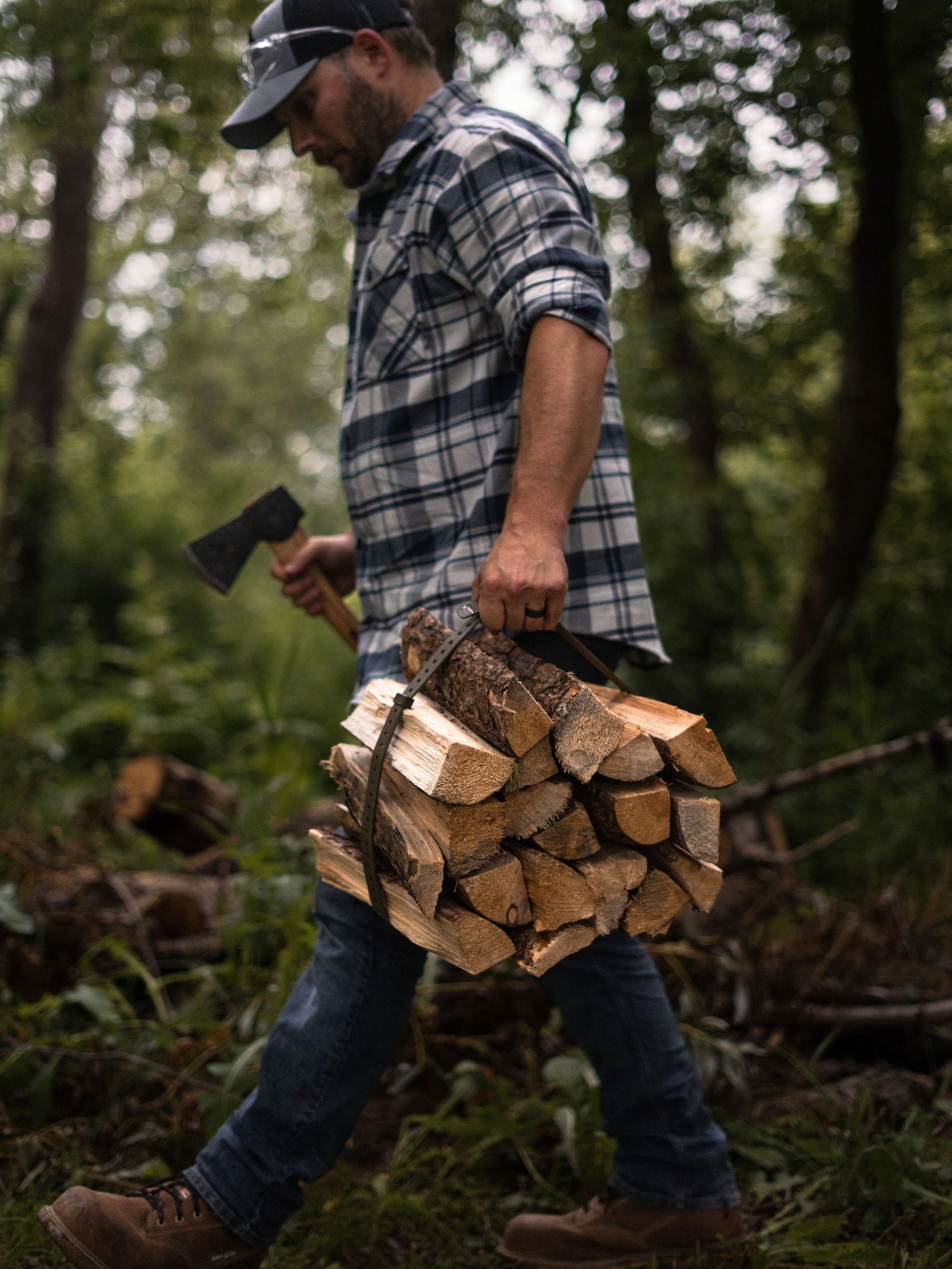 Person carrying firewood through a wooded forest area.