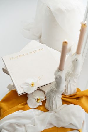 Elegant white photo album with candles and floral accents arranged on yellow silk fabric.