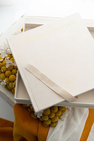 Elegant white gift boxes with gold lettering stacked alongside yellow craspedia flowers and orange velvet ribbon.