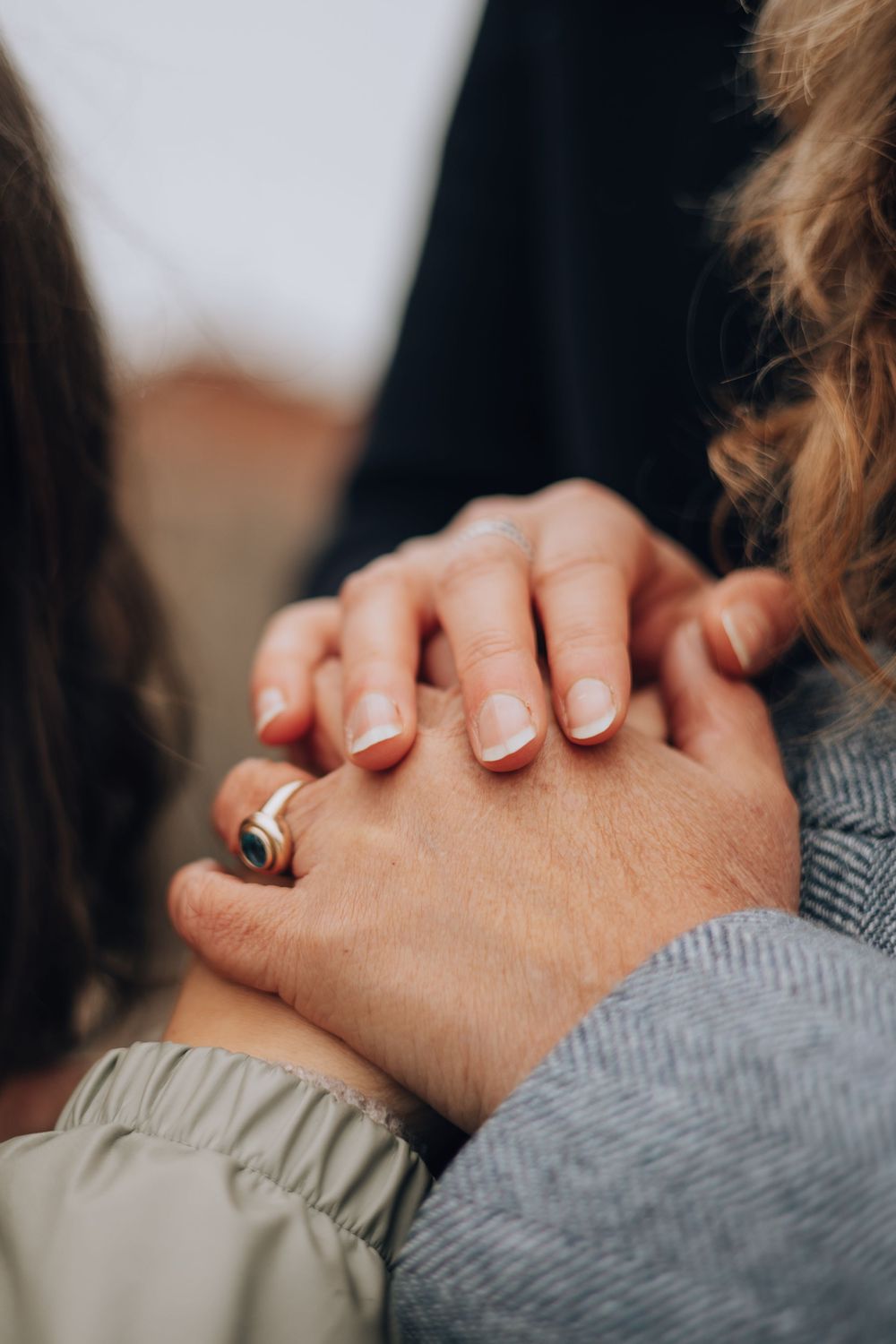 Close-up of three women holding hands together, one wearing a distinctive ring.