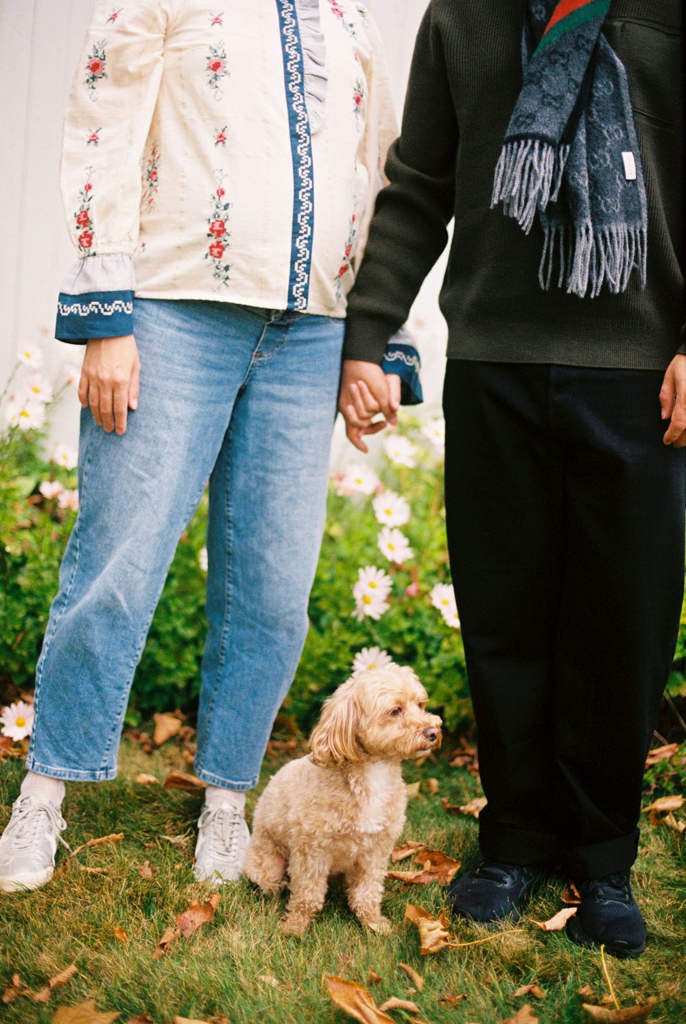 Holding hands in front of the wildflowers with their little dog loyally staying below in the grass during a maternity film photoshoot.