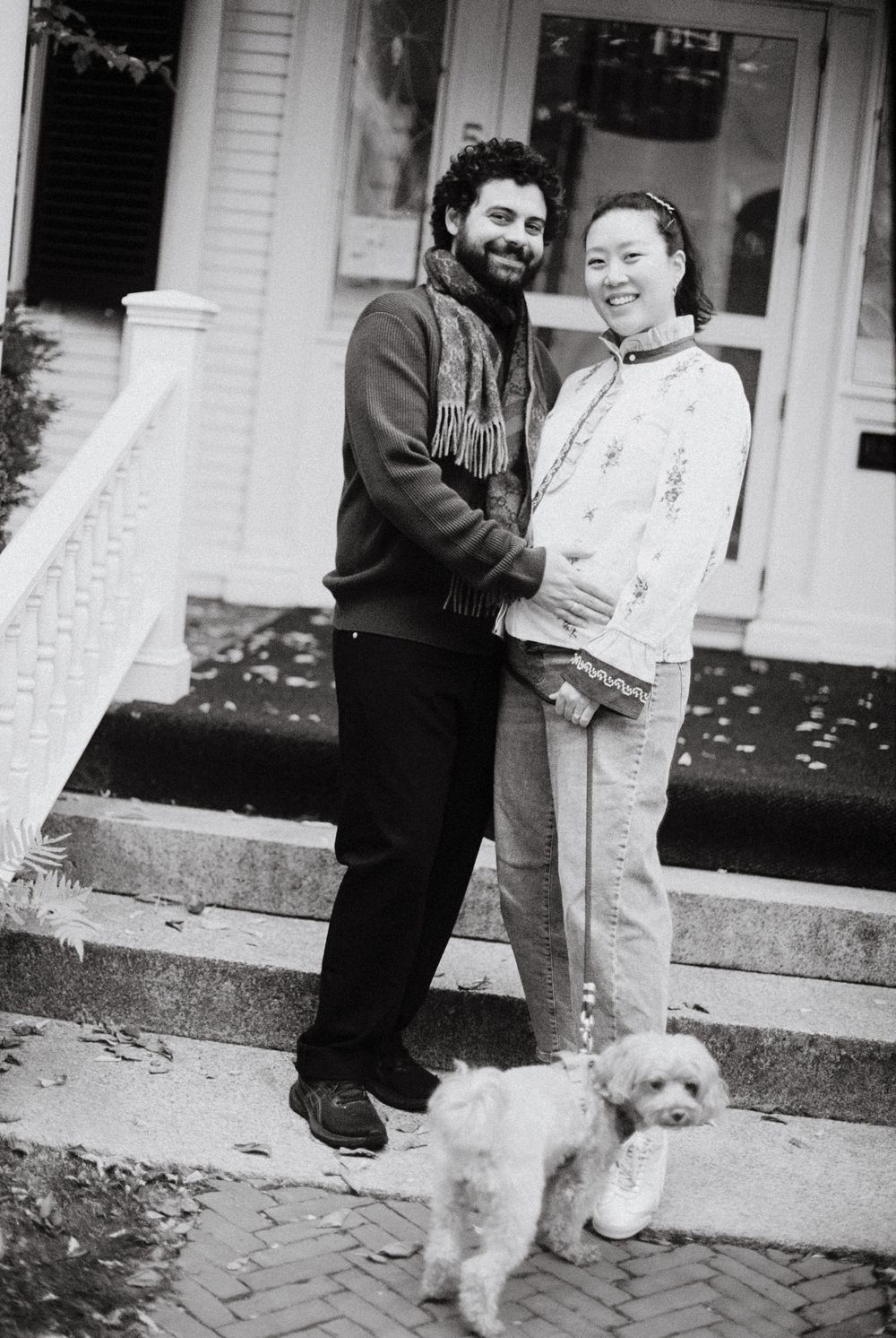 Black and white film photograph of a happy couple expecting a baby during their mini-moon along with their small sweet dog.