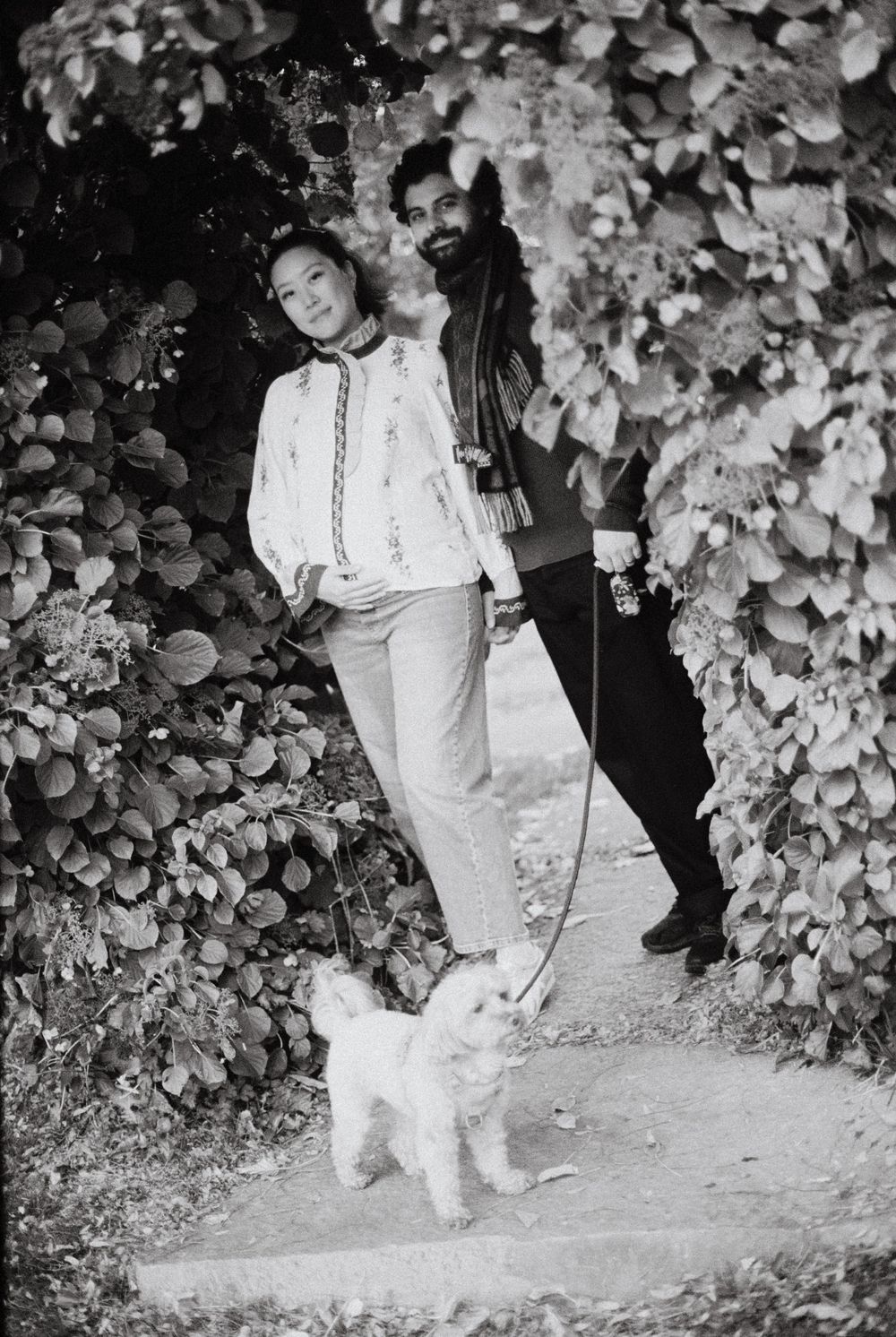 Black and white film photograph of couple smiling together beneath an ivy covered archway outside in the sunshine in Kennebunkport, Maine.