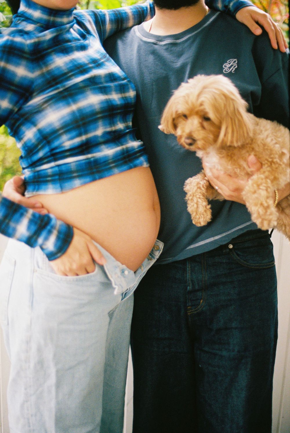Couple embraces and also hold their little dog to celebrate their growing family outside a hotel in Kennebunkport, Maine.