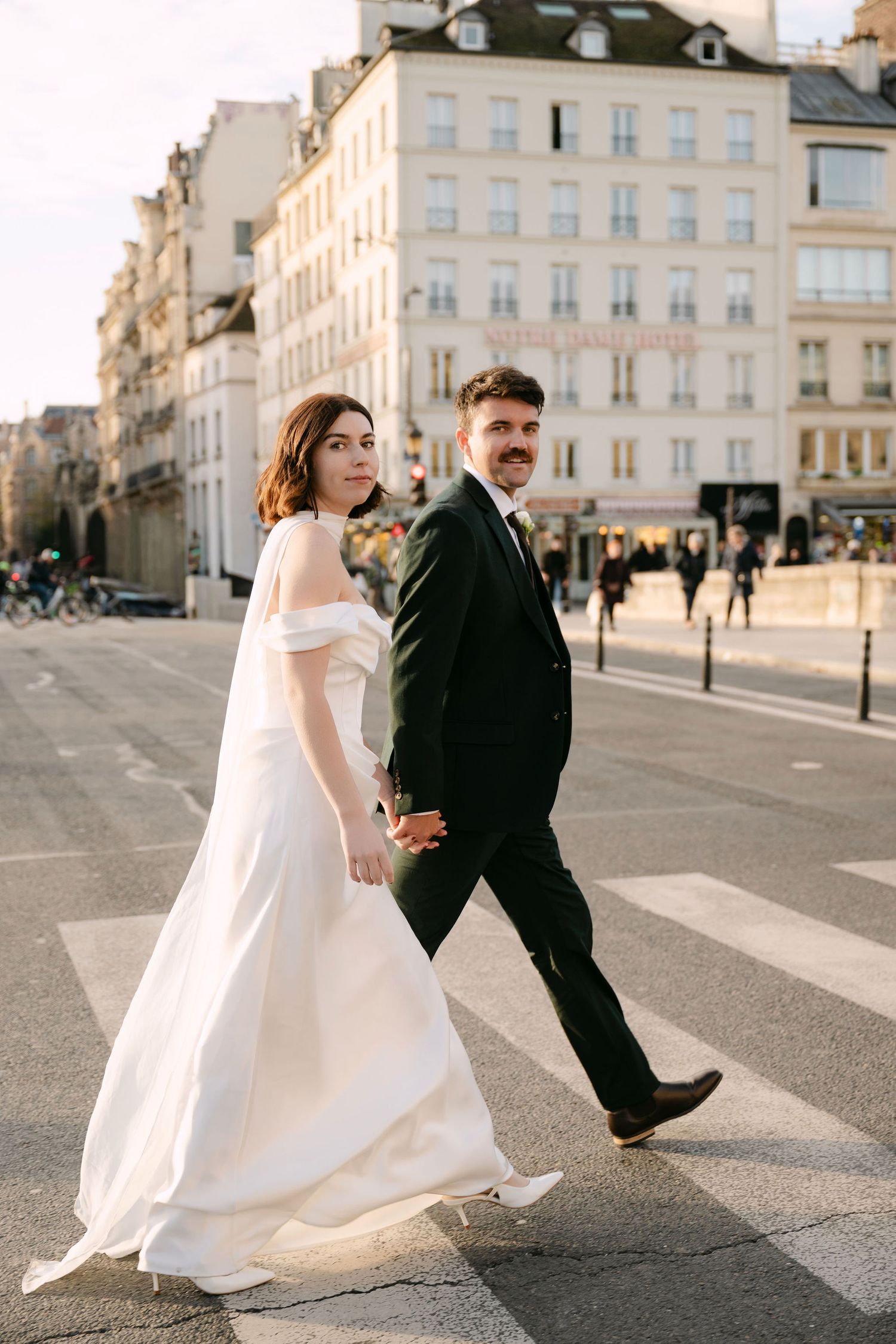 A couple in wedding attire poses together on a cobblestone street in Paris with elegant buildings in the background.