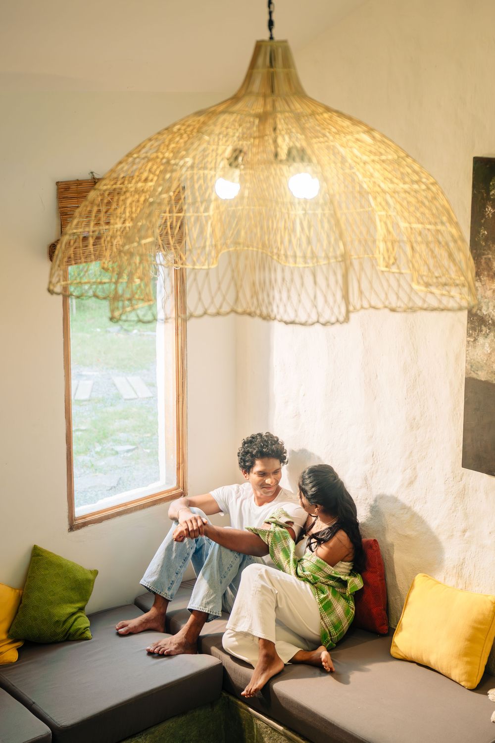 Cozy seating area with woven lamp shade, yellow pillows and window view.