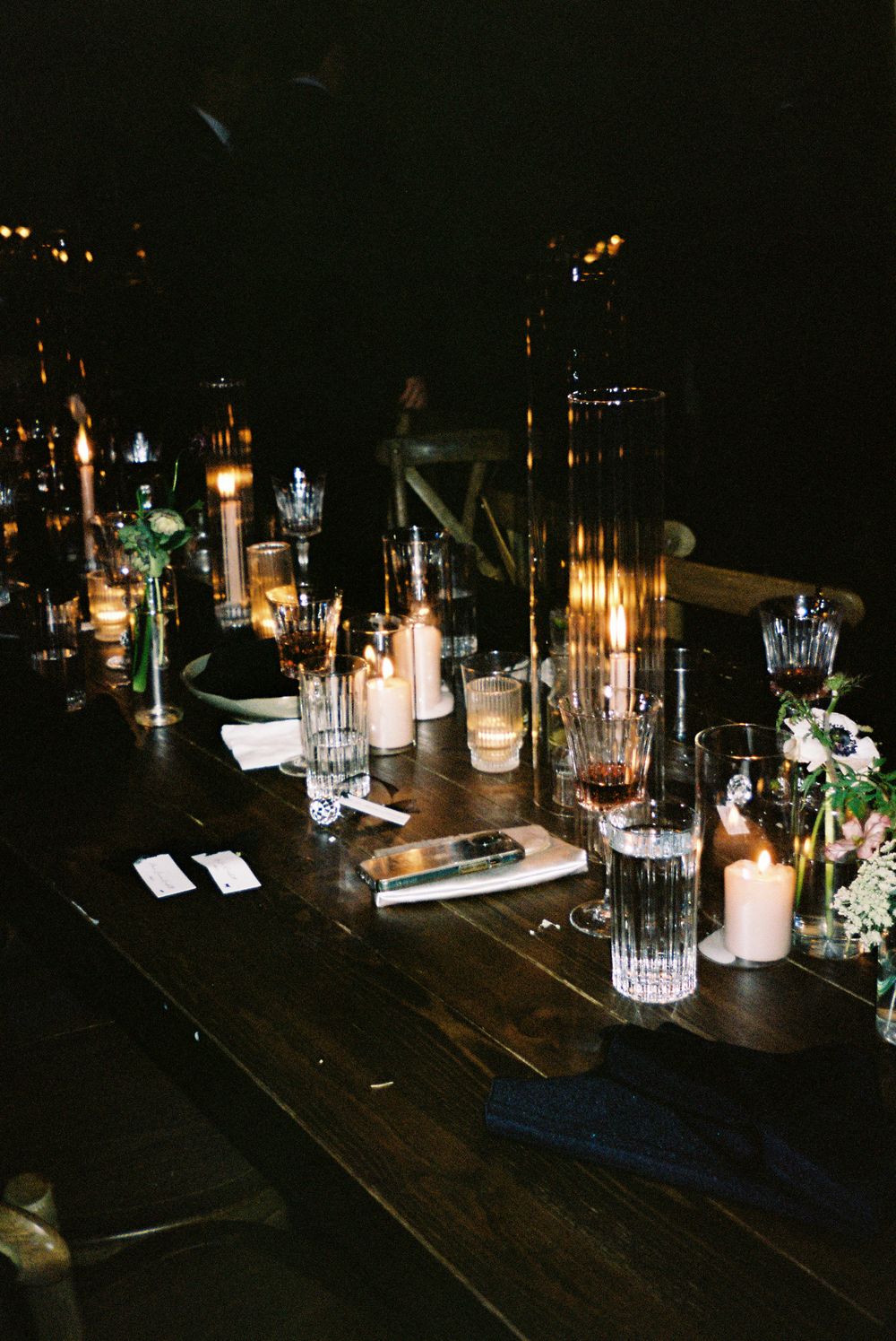 Elegant table setting with glowing candles and crystal glassware on dark wooden surface at night.