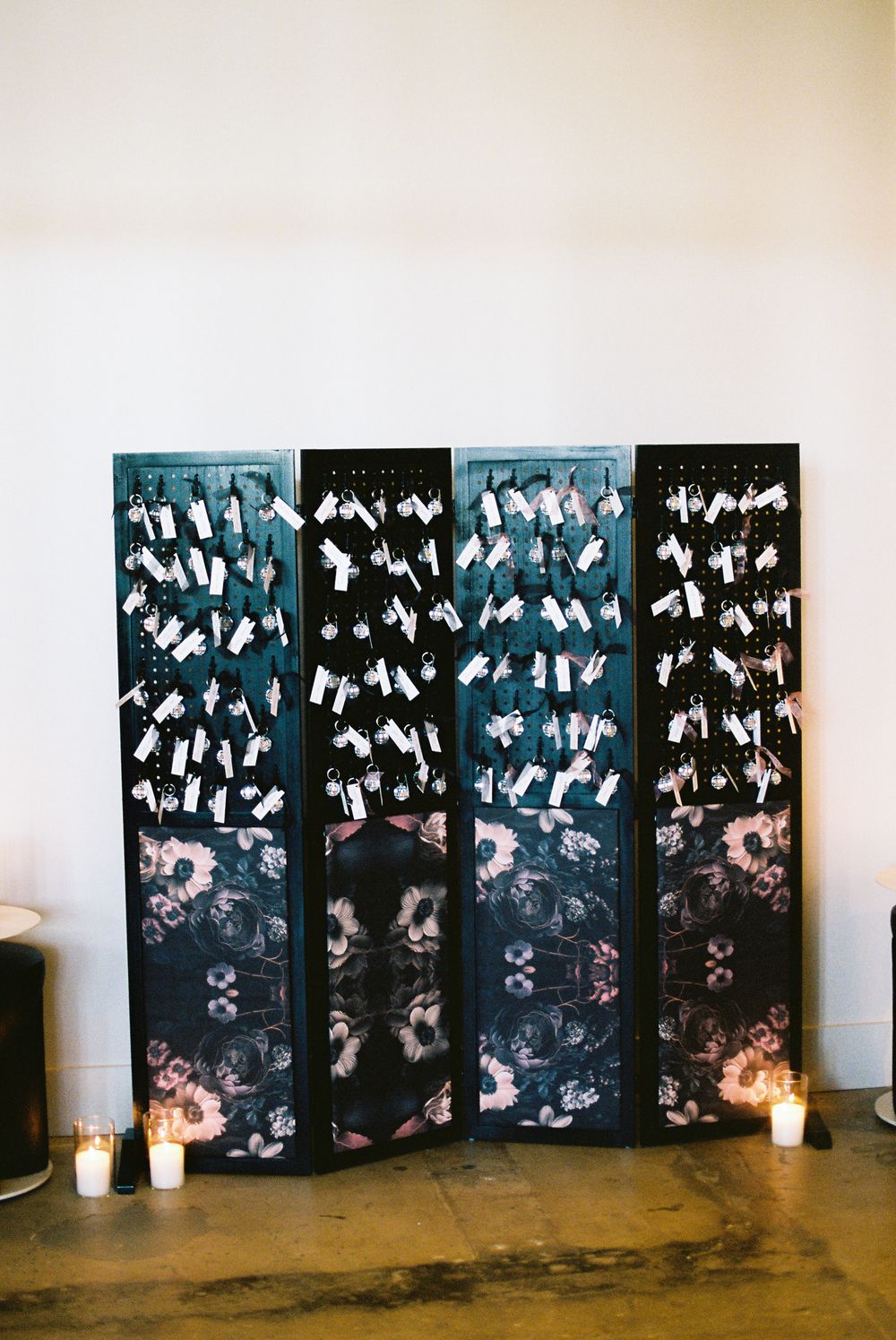 Artistic black panels with white floral patterns arranged against a white wall with candles at the base.