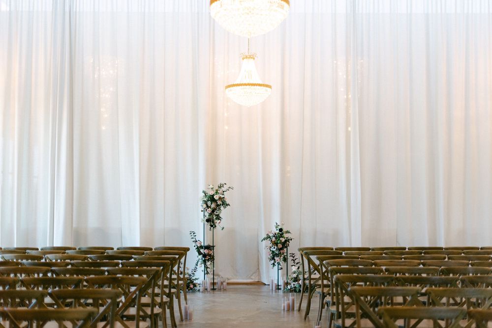 Elegant wedding ceremony setup with rows of wooden chairs and white drapes in a minimalist indoor venue.