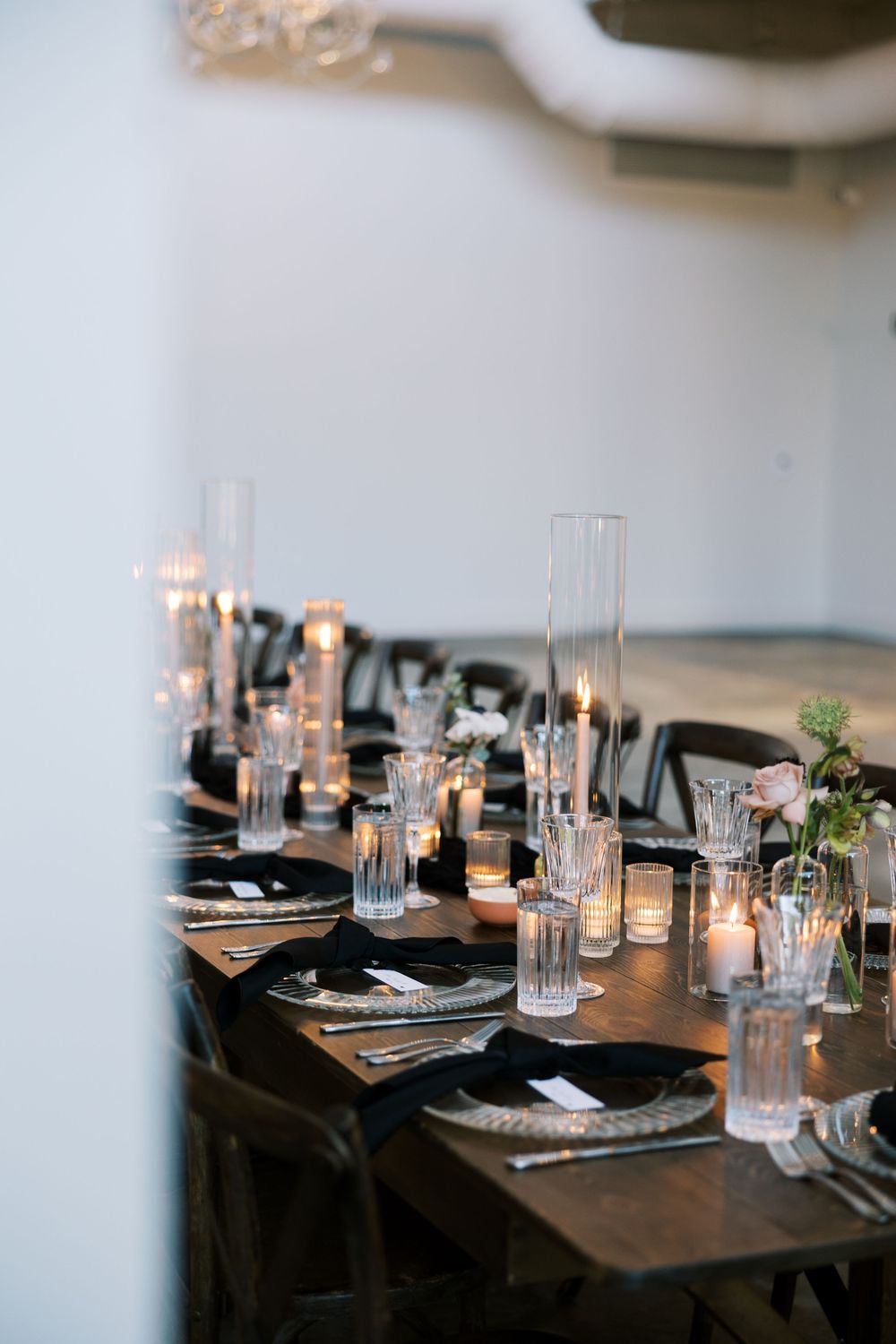 Modern table setting with black chairs, tall glass vases, and candlelight for an elegant dinner event.