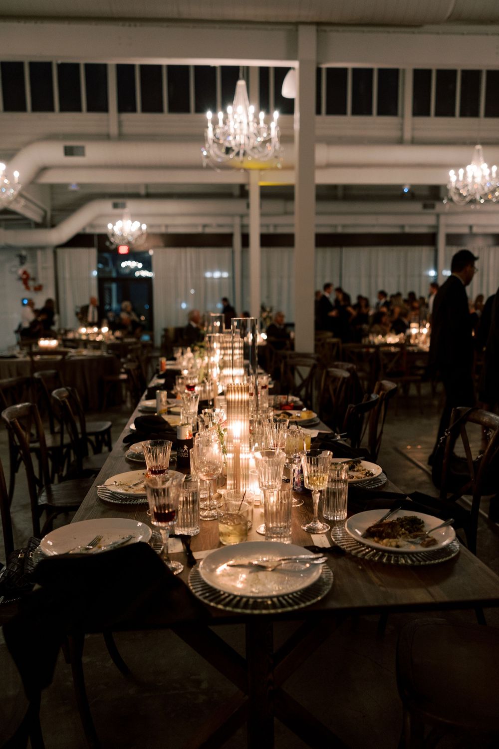 Elegant wedding reception tables set with glowing candles and crystal chandeliers in a dimly lit venue.