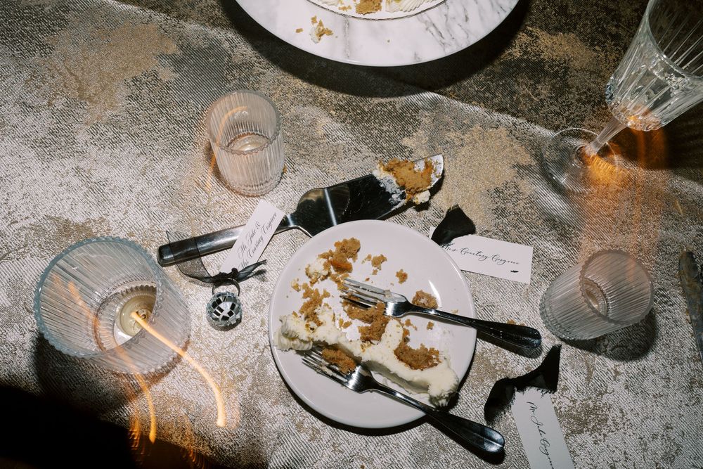 Wedding reception table aftermath with empty plates, glasses and scattered cake crumbs.