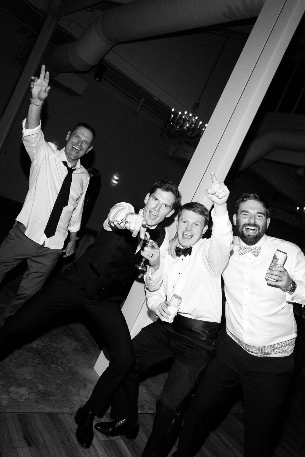 Black and white photo of wedding guests dancing and celebrating with raised arms on the dance floor.