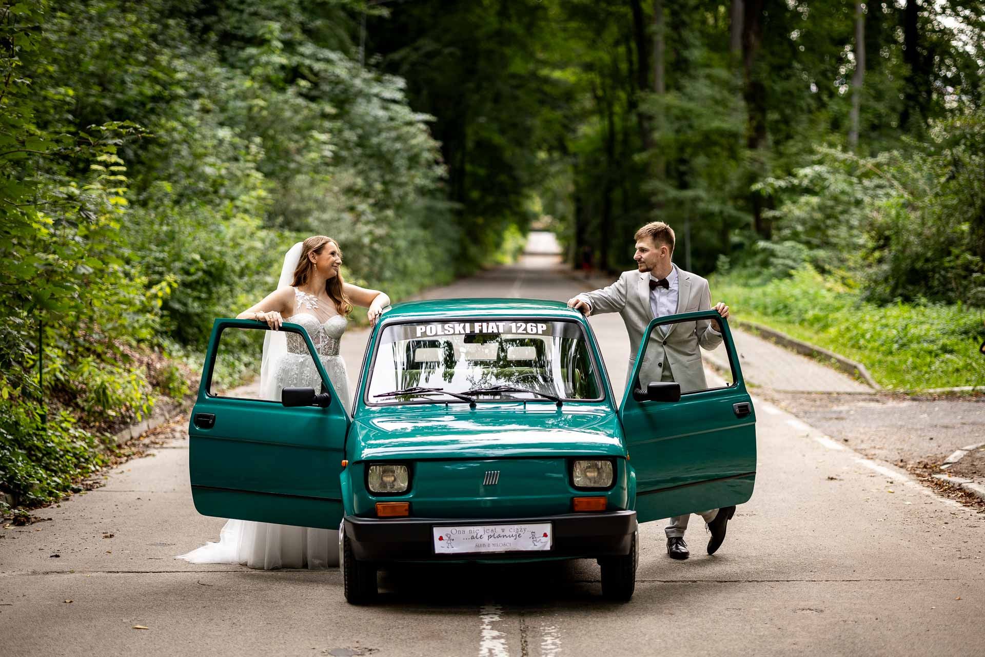 A romantic wedding photoshoot with a vintage teal car on a tree-lined path.