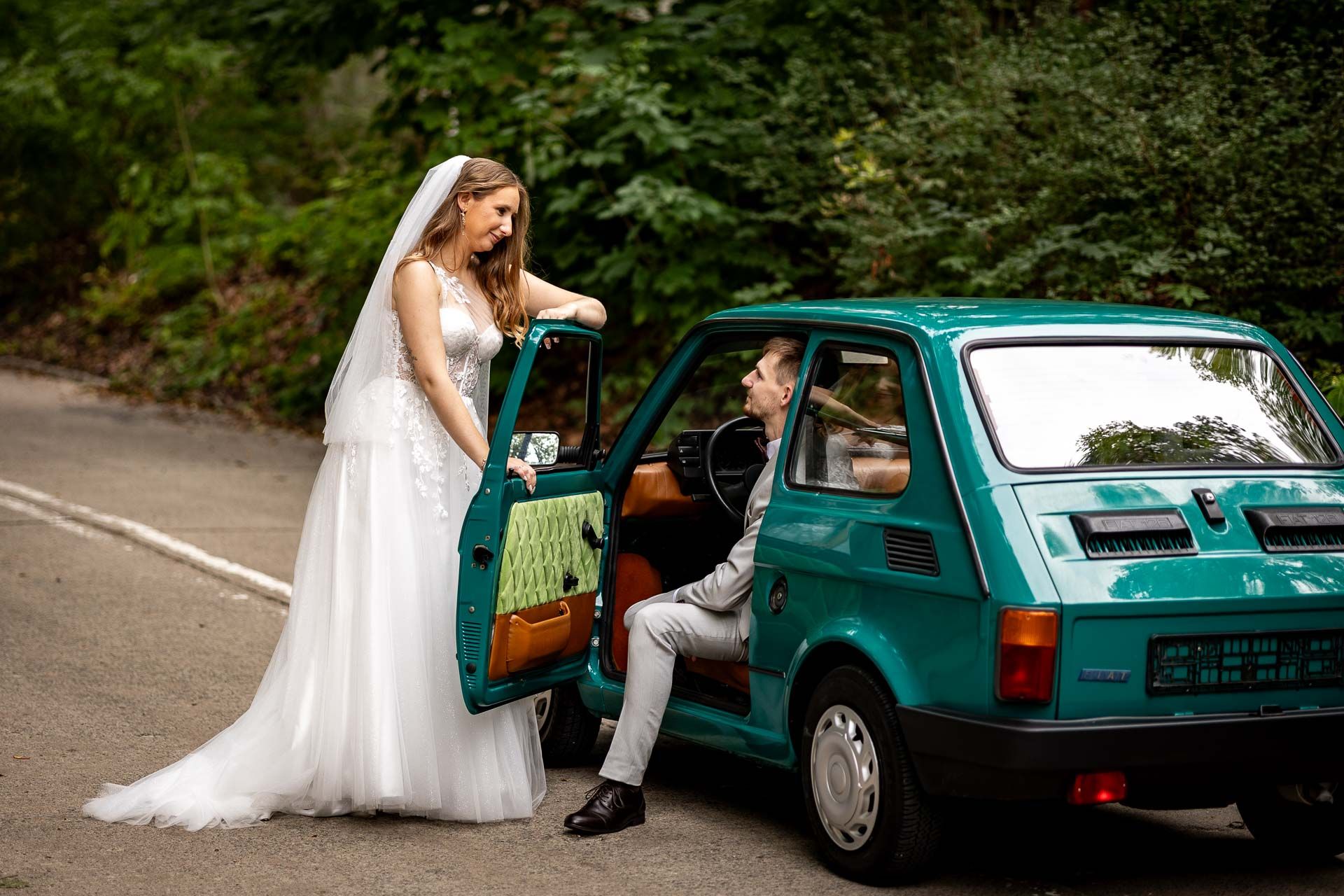 Elegant wedding portraits with a retro teal car in a wooded setting.