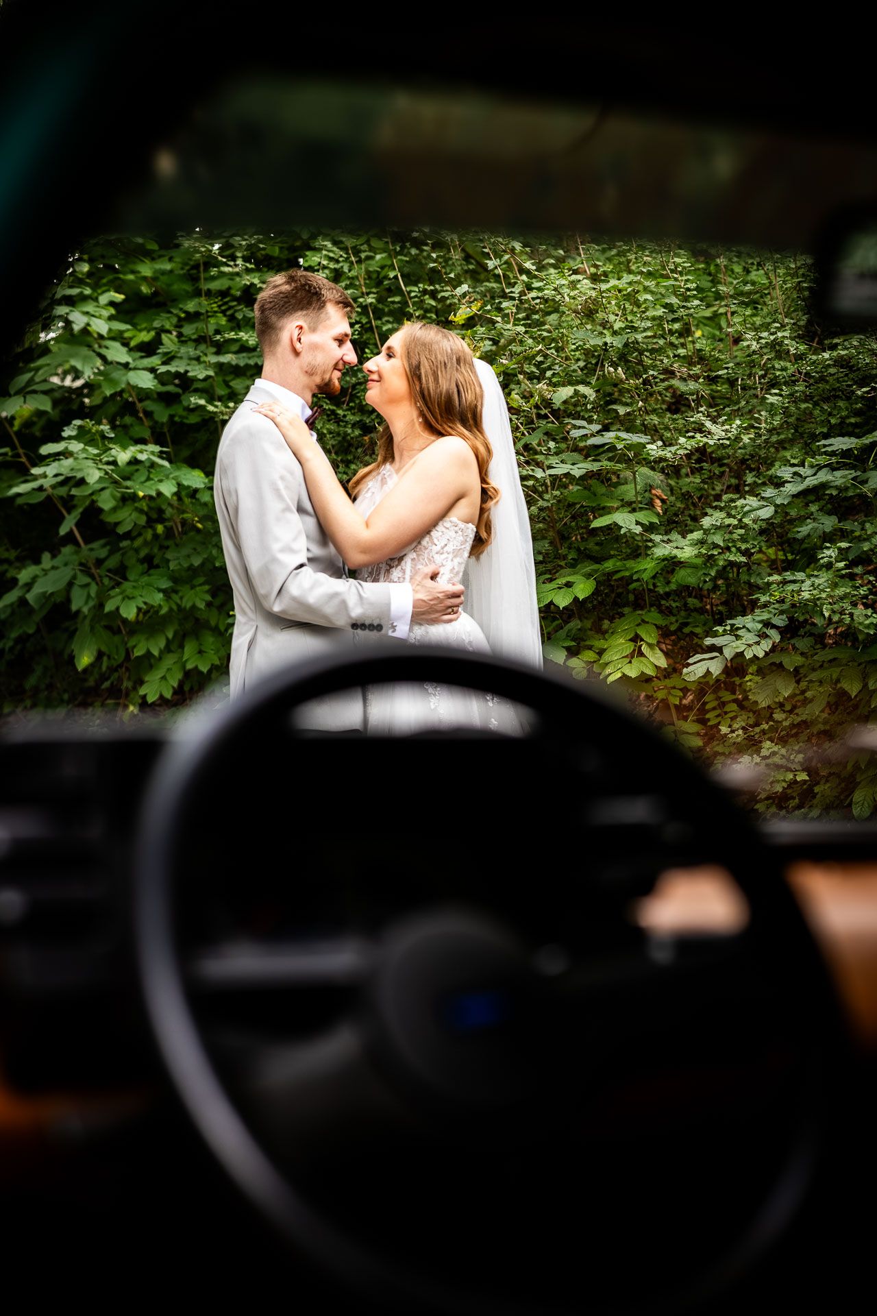 Artistic wedding photography through car window with greenery background.