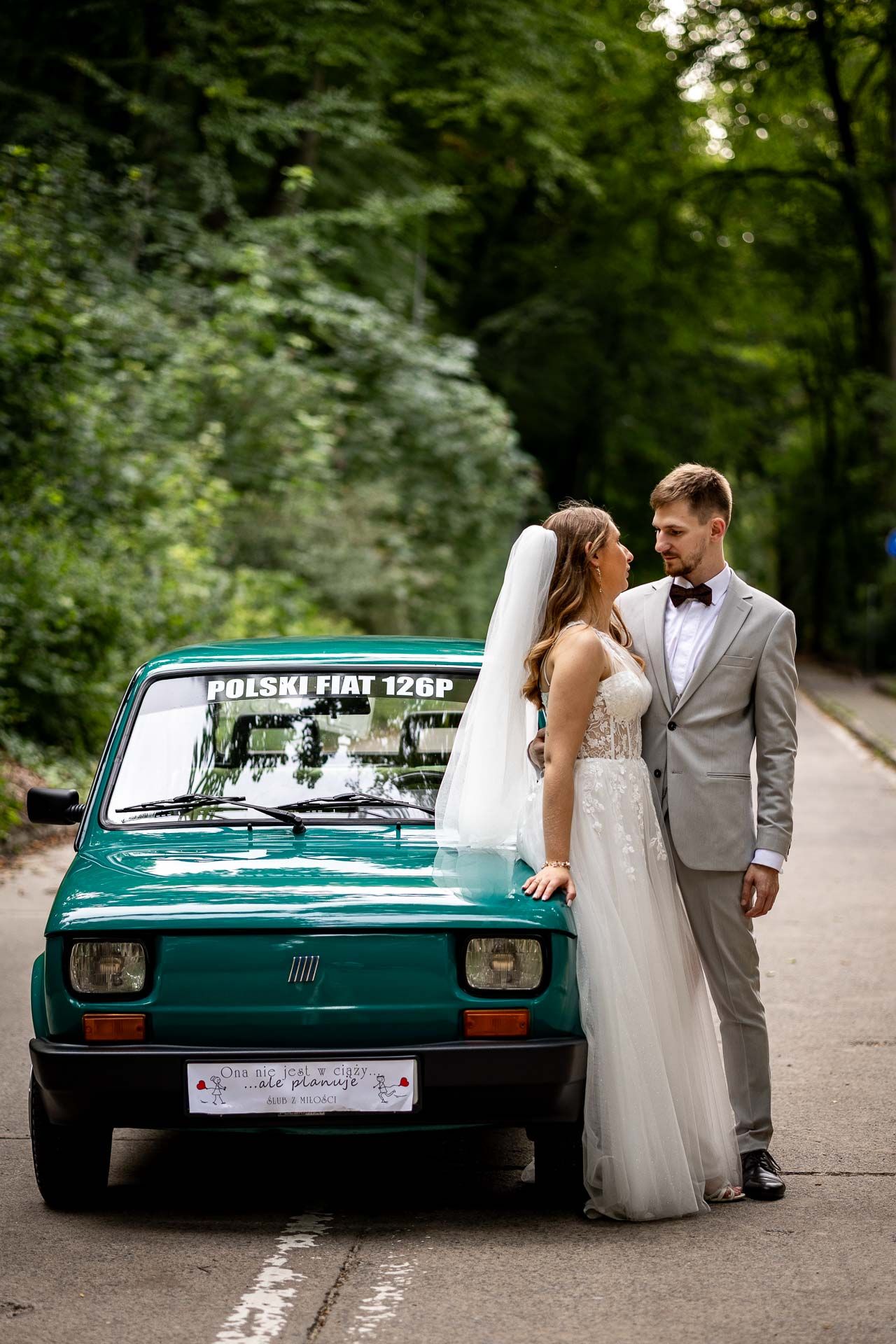 Romantic wedding portraits with classic teal Fiat on forest path.