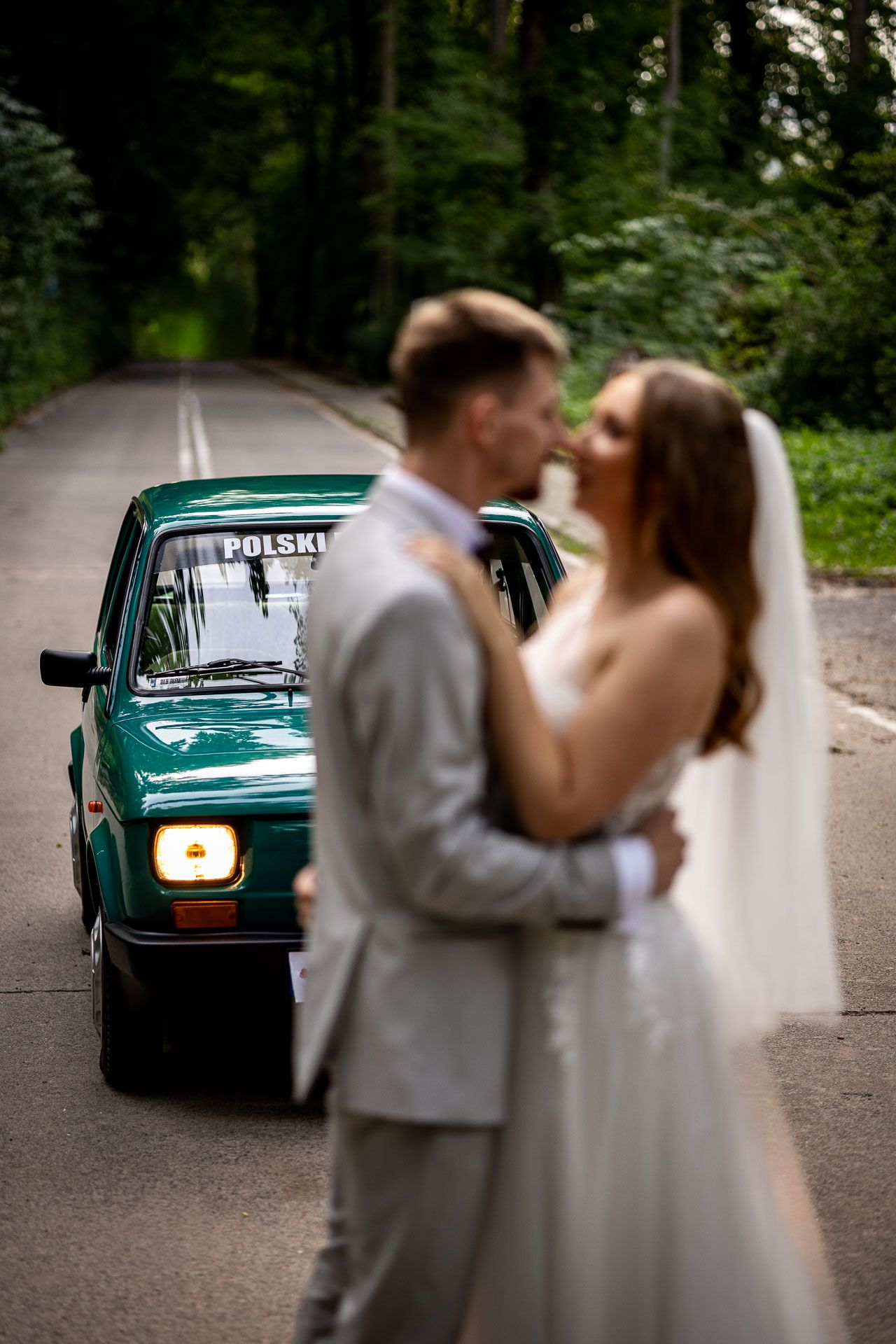 Wedding couple shares intimate moments near vintage teal car.
