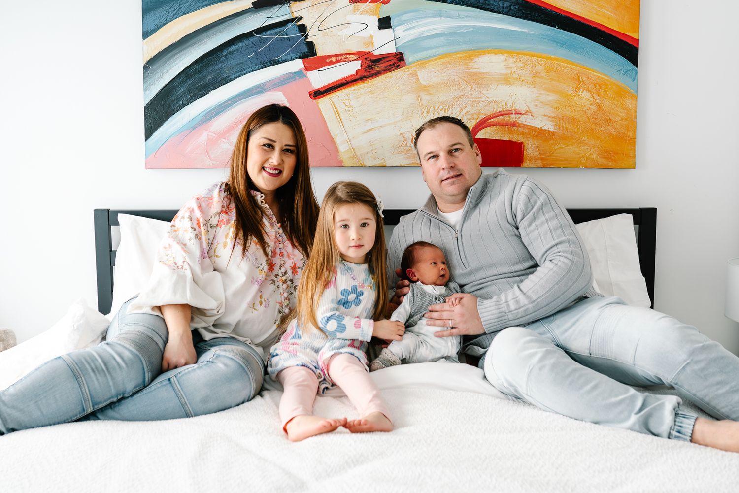 Family lounges together on white bedding taken during an in-home newborn family photo session in Melbourne.