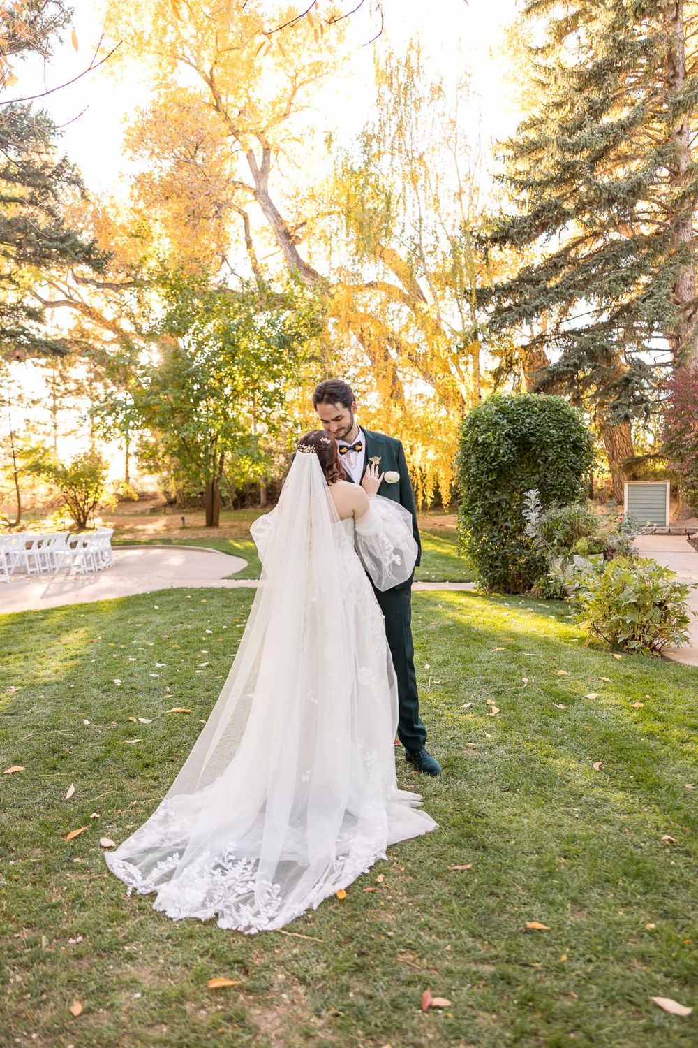 Couple shares romantic moment in autumn garden with golden sunlight filtering through trees as bride's lace dress trails behind.
