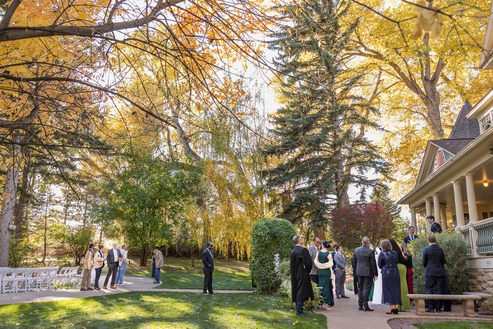 A group gathers outside on a lawn surrounded by autumn trees with golden leaves near a building entrance.