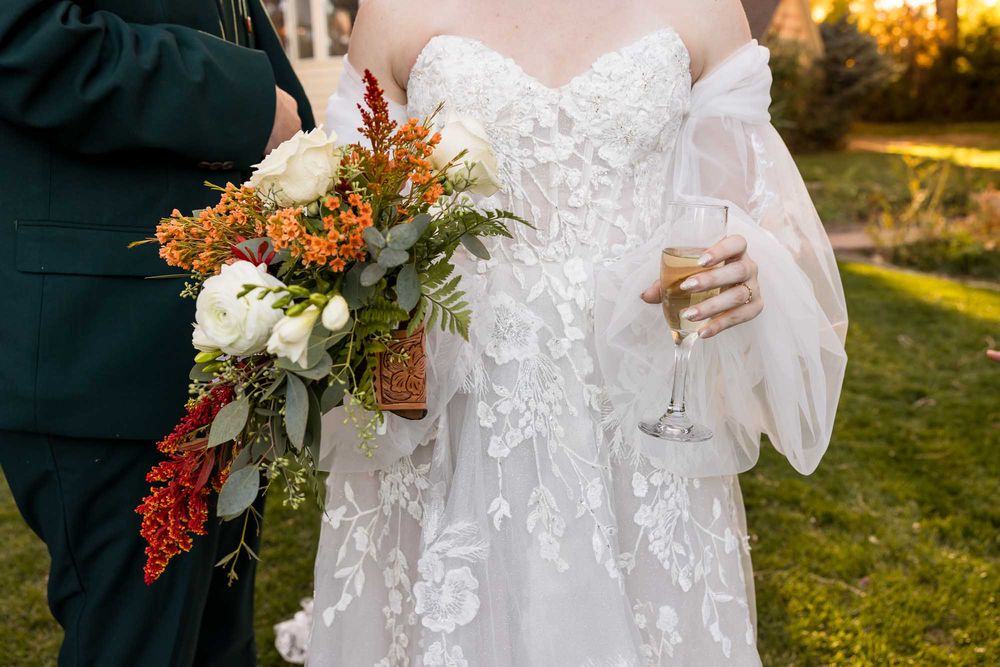 Close-up details of white lace wedding dress and autumn-themed floral bouquets during an outdoor ceremony.