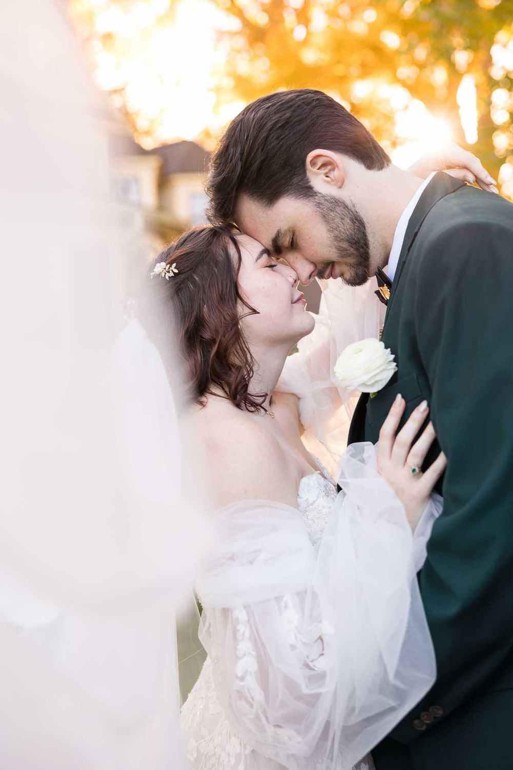 Romantic wedding couple embraces in warm sunset light with autumn foliage in background.