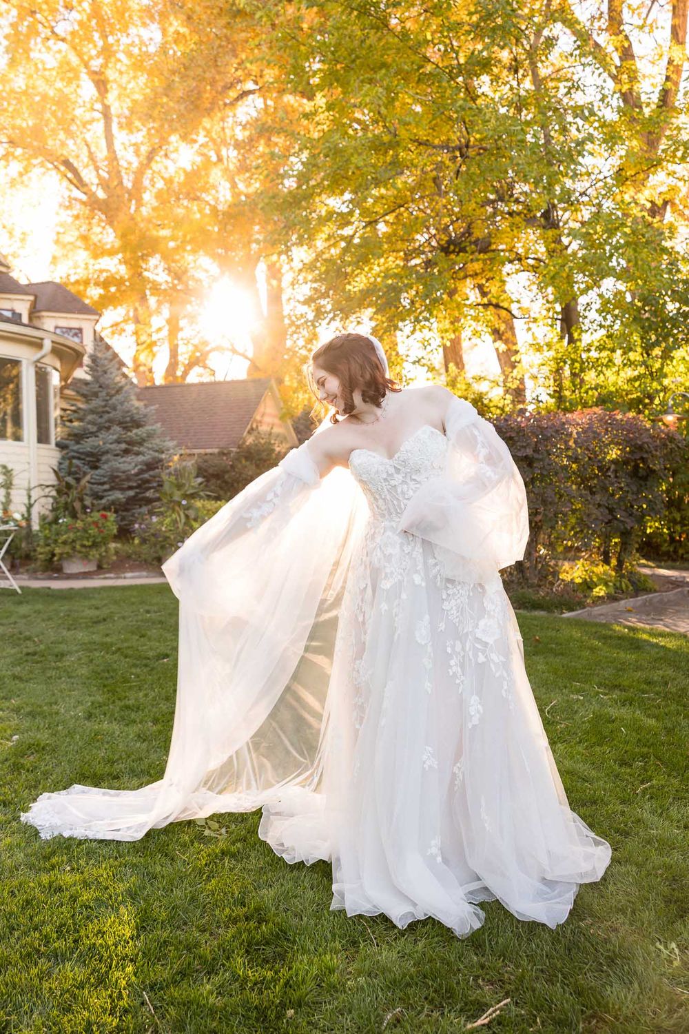 A flowing white wedding dress twirls gracefully in golden sunlight on a grassy lawn during sunset.