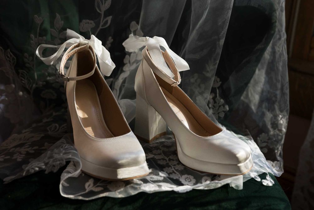 Elegant white bridal shoes with delicate lace details against a dark dramatic background.