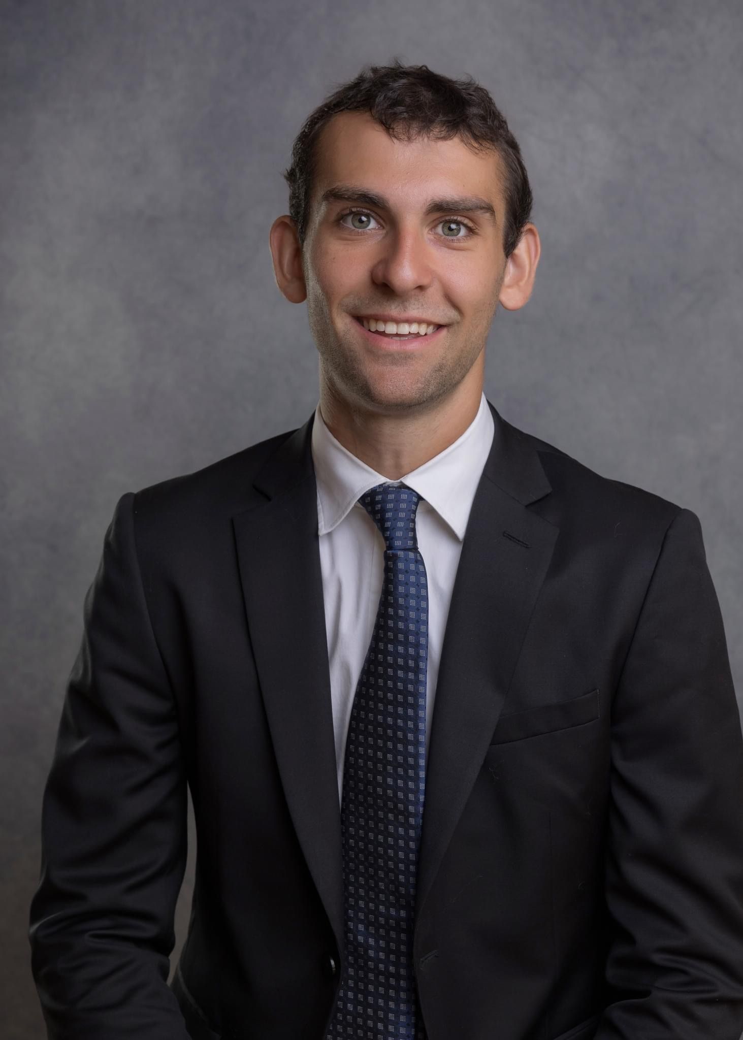 Professional headshot series showing different expressions in a dark suit and blue tie against a gray background.