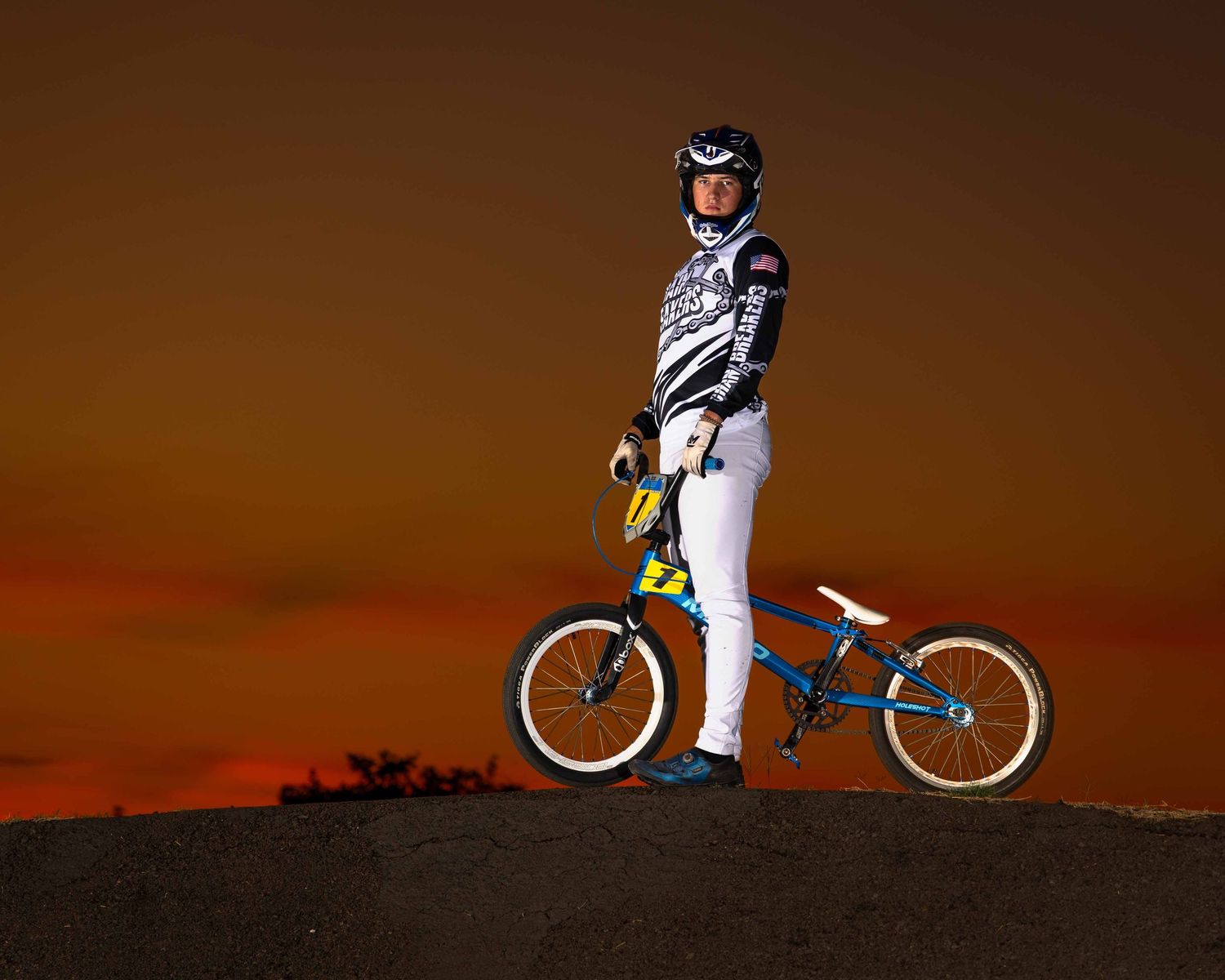 A BMX rider performs a trick sequence against a dramatic orange sunset sky backdrop.