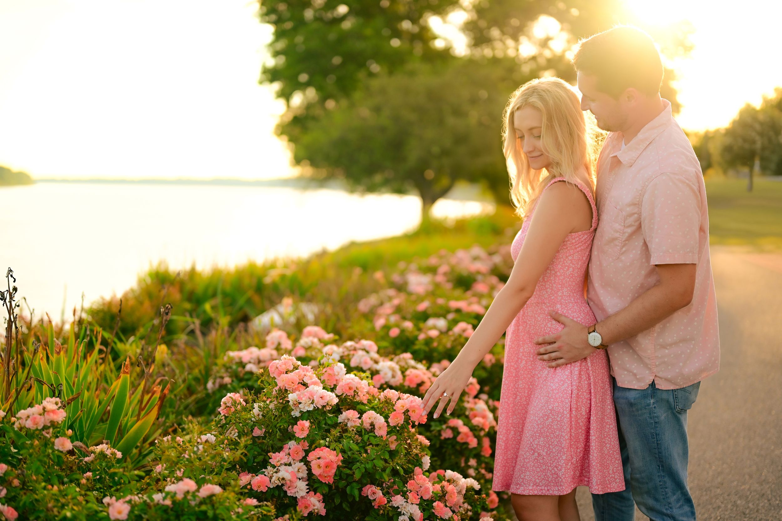 Romantic couple embraces at sunset in a garden filled with pink flowers and golden sunlight.