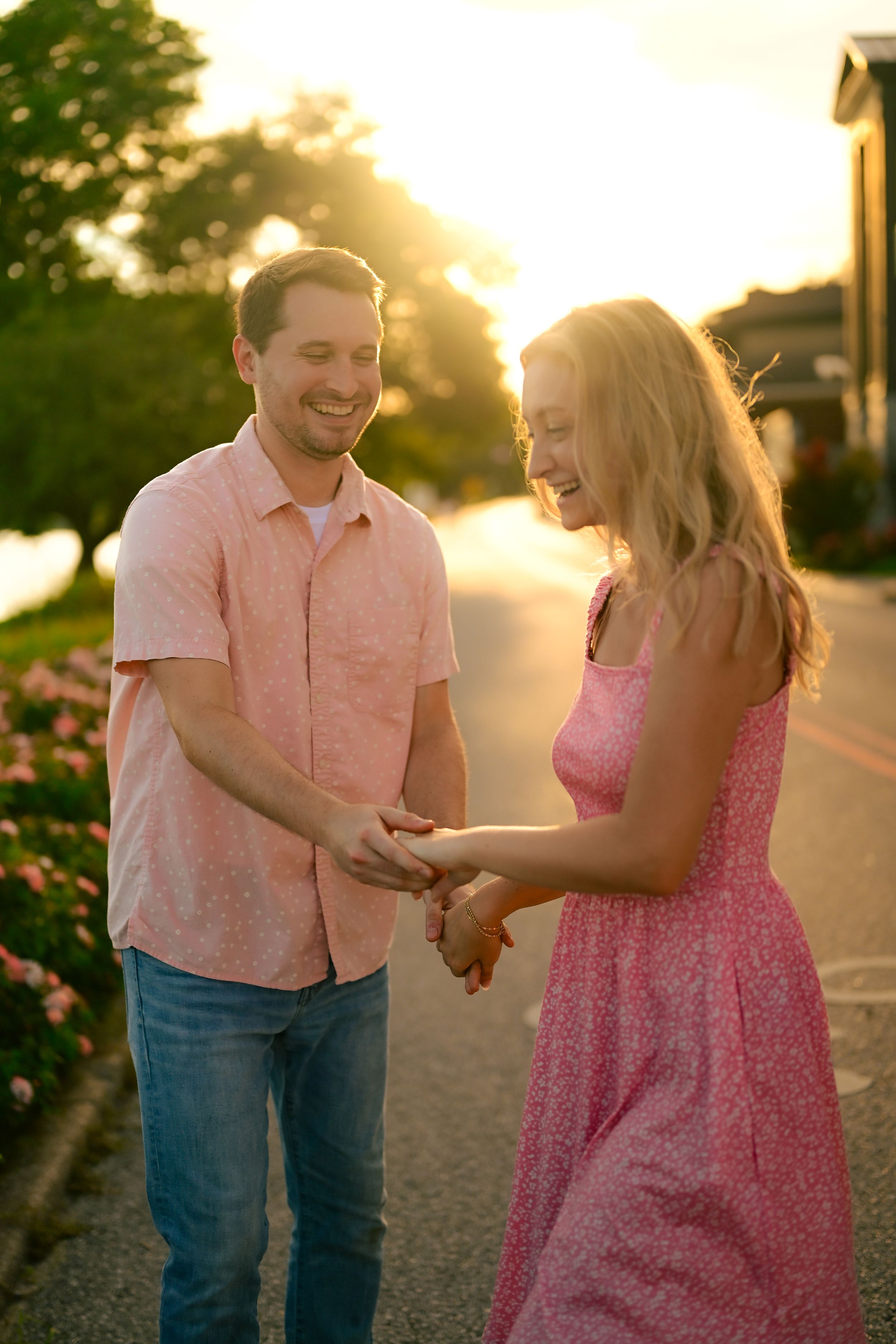 A romantic couple shares a playful moment at sunset on a flower-lined walkway.