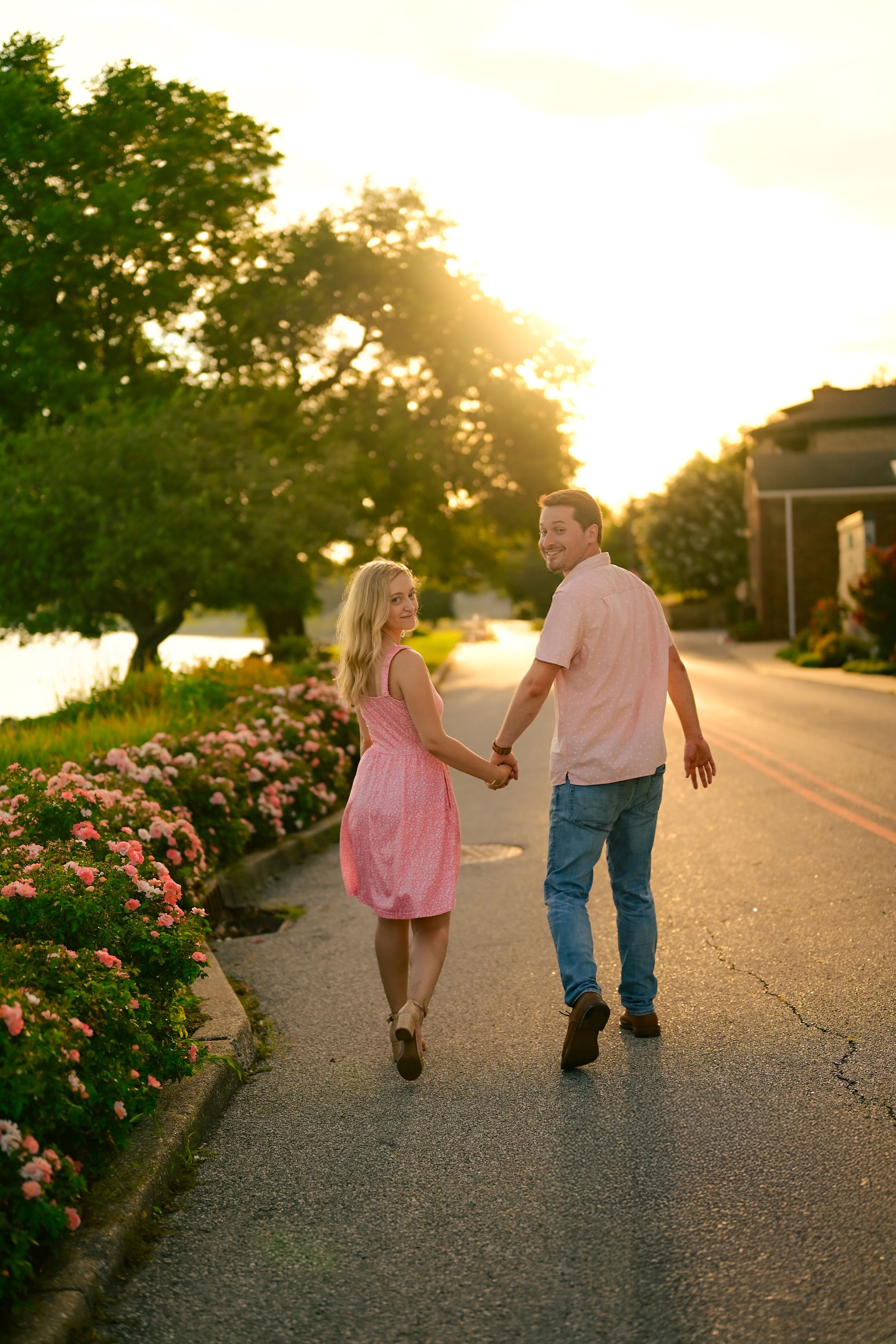 Two people walk hand in hand down a sunset path with blooming roses.