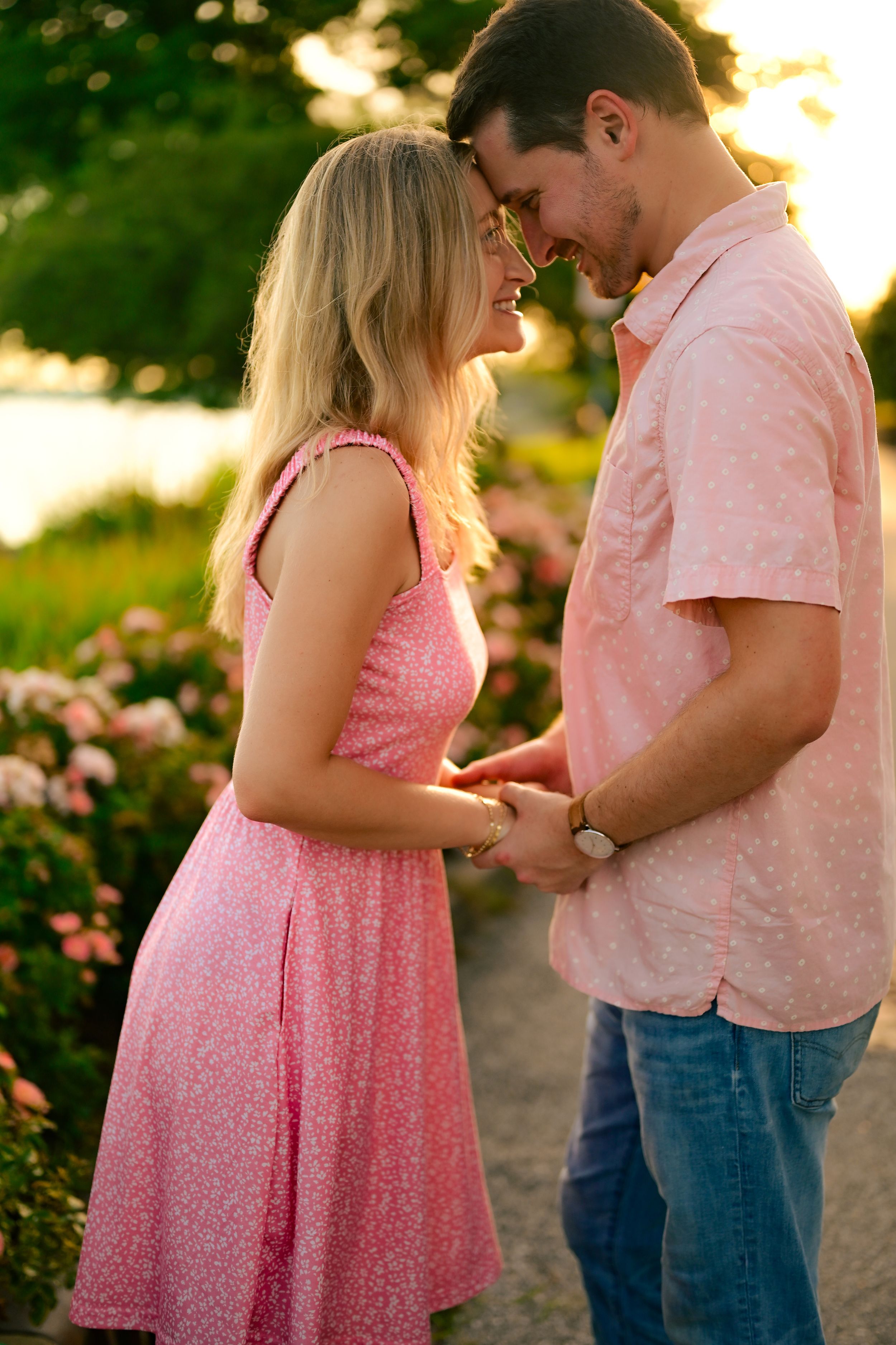 A couple shares a tender moment outdoors at golden hour, coordinating in pink outfits among blooming flowers.