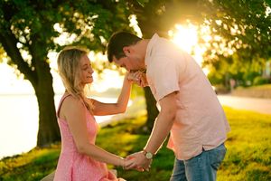 Couple embraces in a romantic sunset moment under green trees in a park setting.