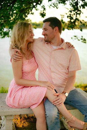 Couple in pink attire sitting together on a bench outdoors during golden hour with trees in background.