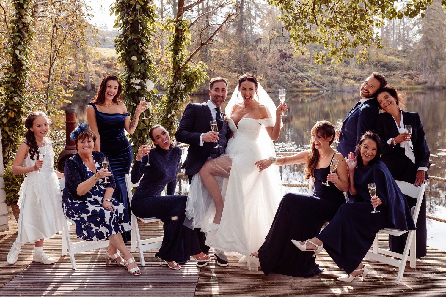 Wedding party relaxes and poses together at Gilpin Hotel and Lake House on white chairs in an outdoor garden setting during golden hour.