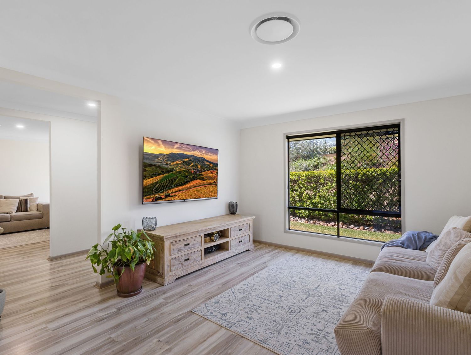 Spacious living area with plush carpet, entertainment unit and natural lighting.