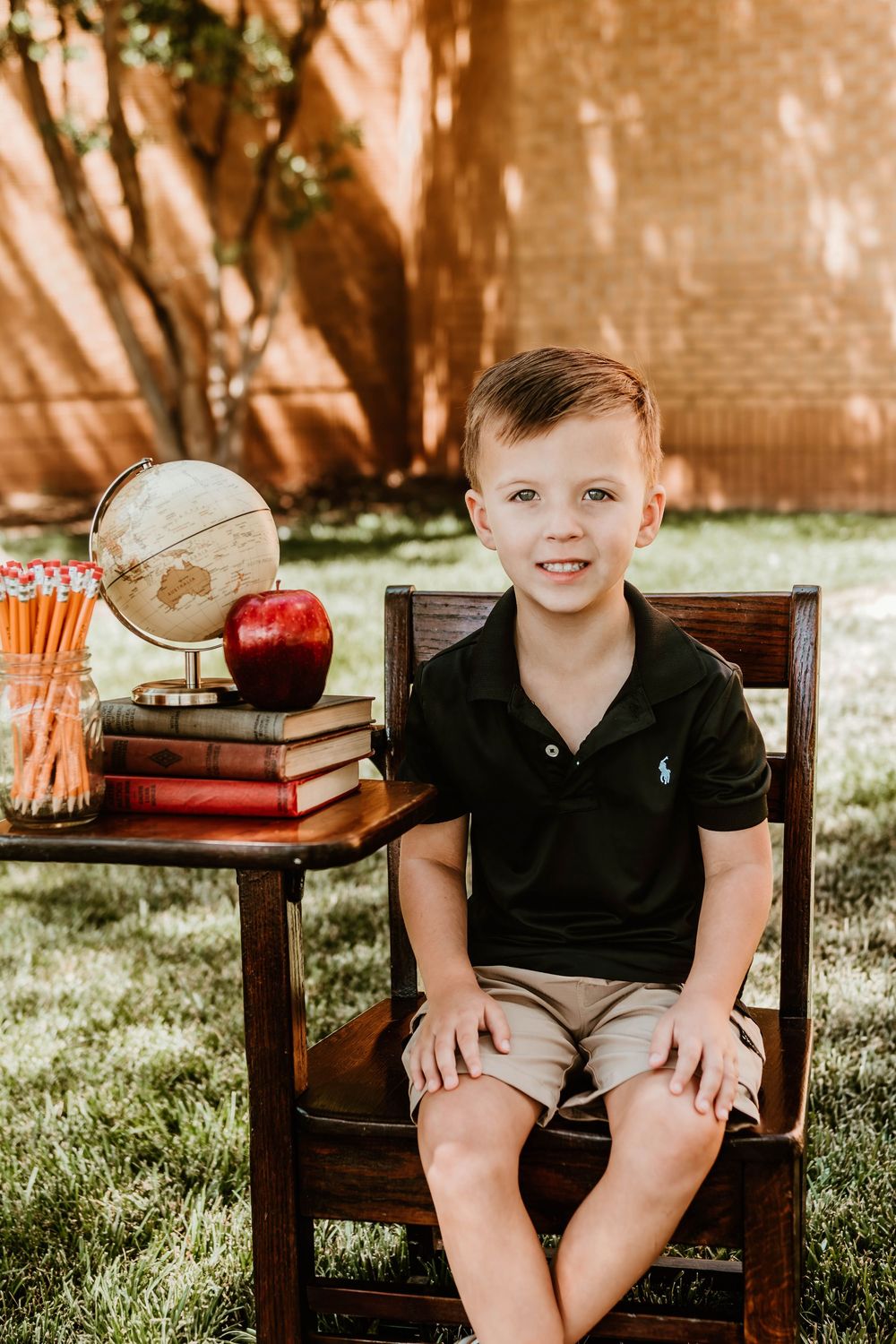 Old books, a red apple, and pencils arranged on a wooden chair outdoors.