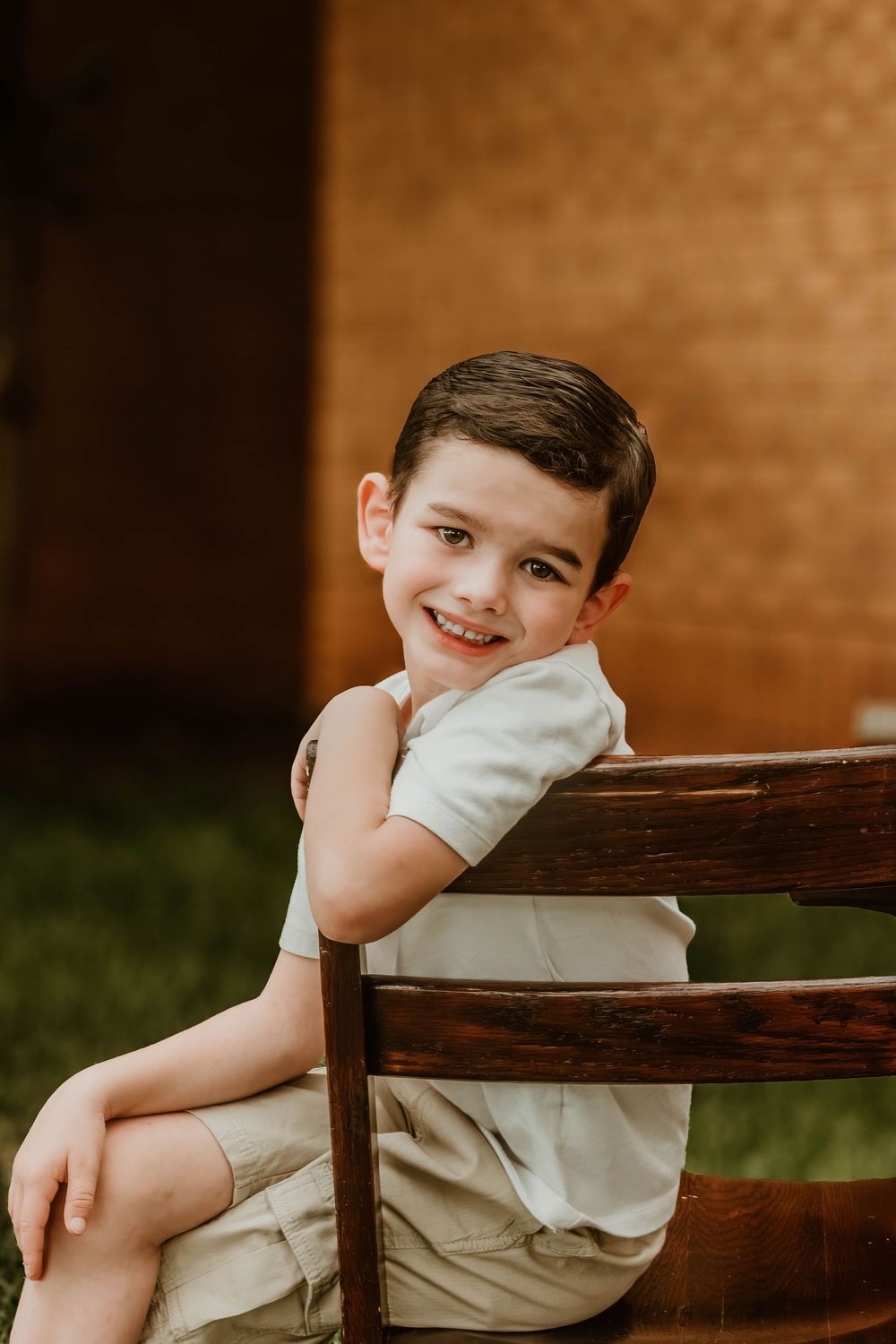 Student poses on wooden chair against brick wall background.
