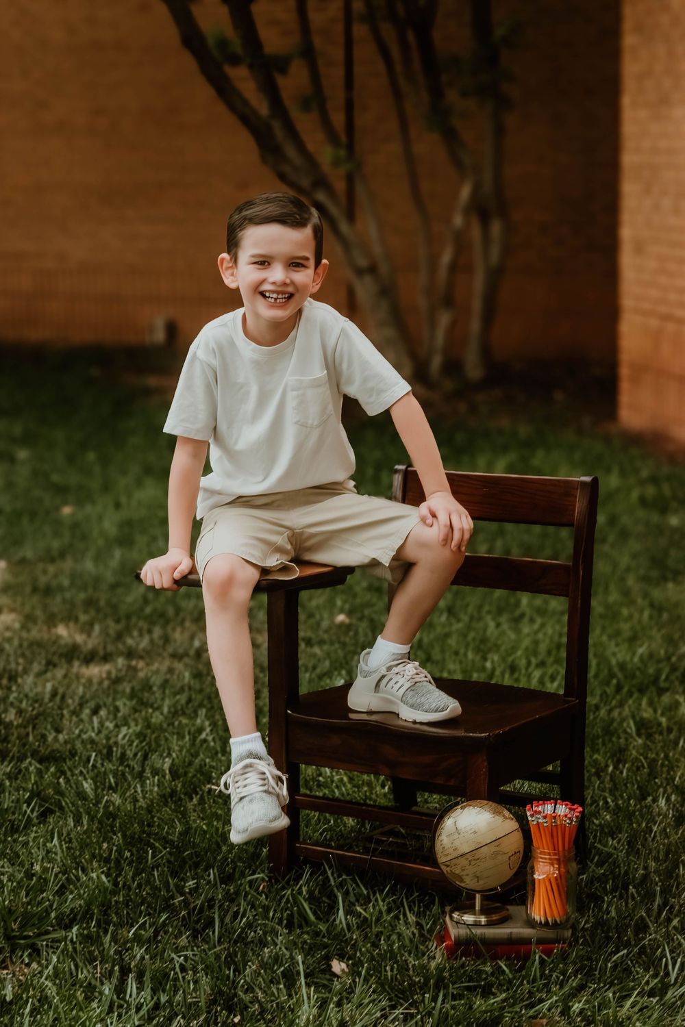 Student sits on wooden chair with globe and school supplies below.