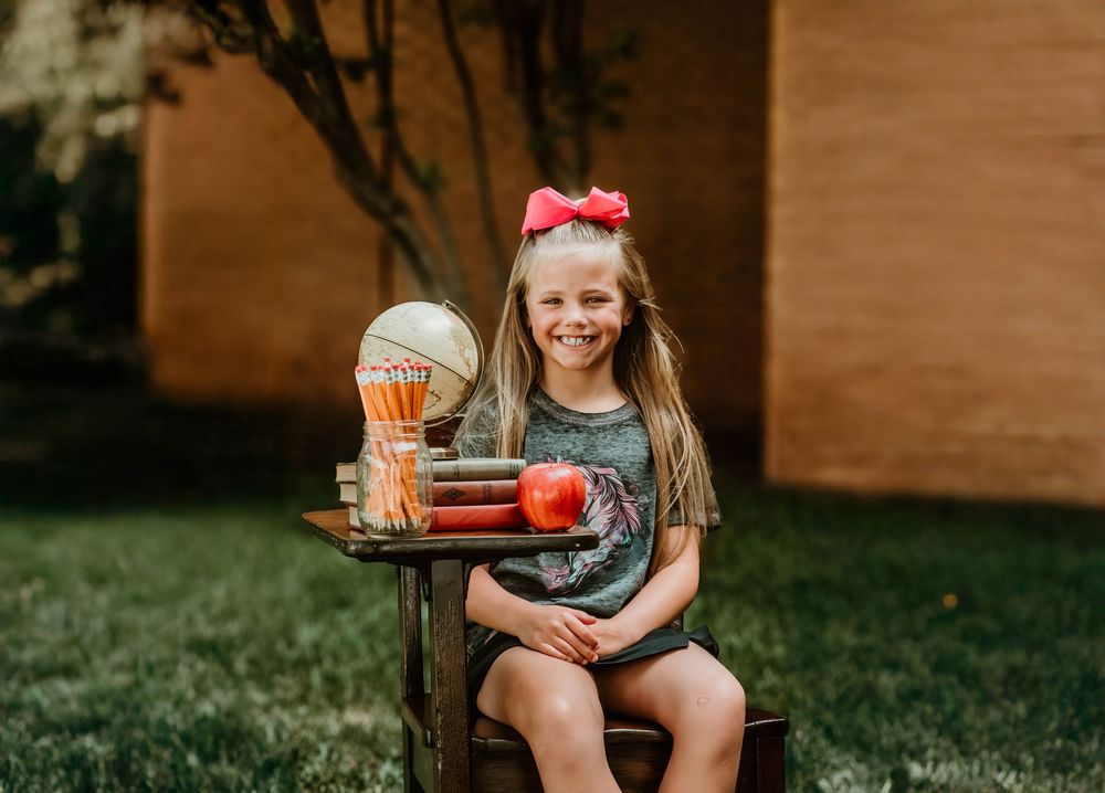 Student sits at wooden desk with globe and apple for back to school photo.