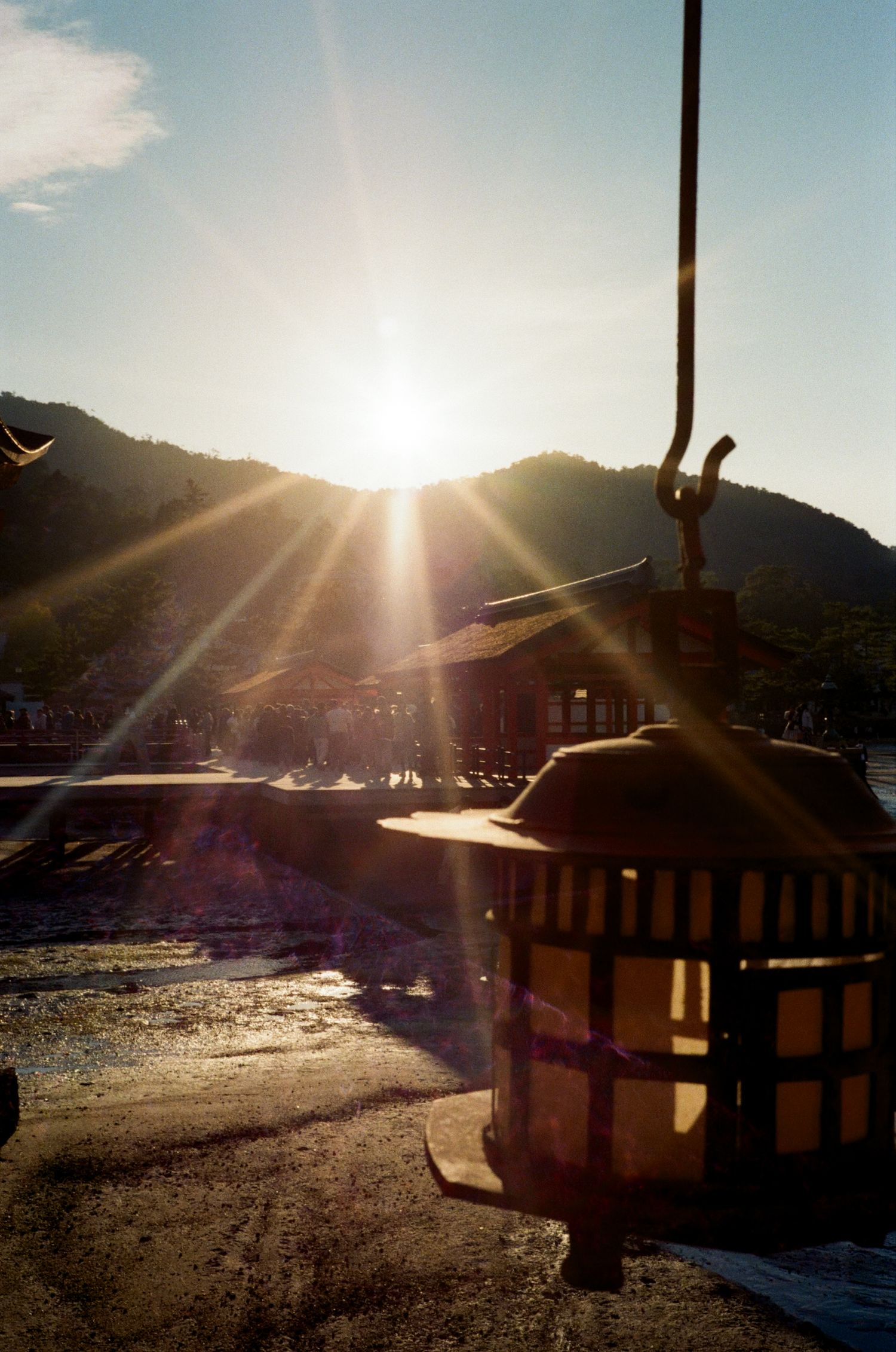 Sunlit ski lift chairs silhouetted against mountain peaks during golden hour with dramatic sun flare in winter landscape.