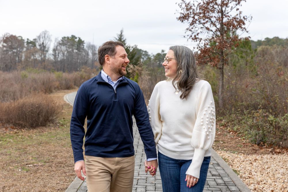 A couple in casual fall attire walks together and laughs while enjoying an autumn day outdoors.