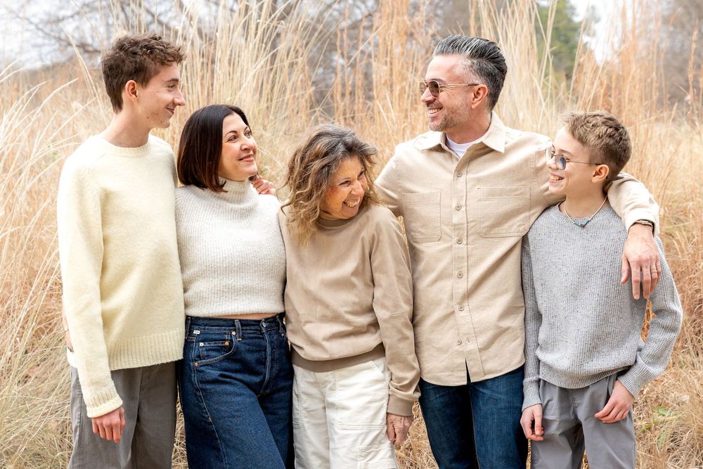 Happy family of five posing outdoors in neutral tones, surrounded by tall dry grass in a natural setting.