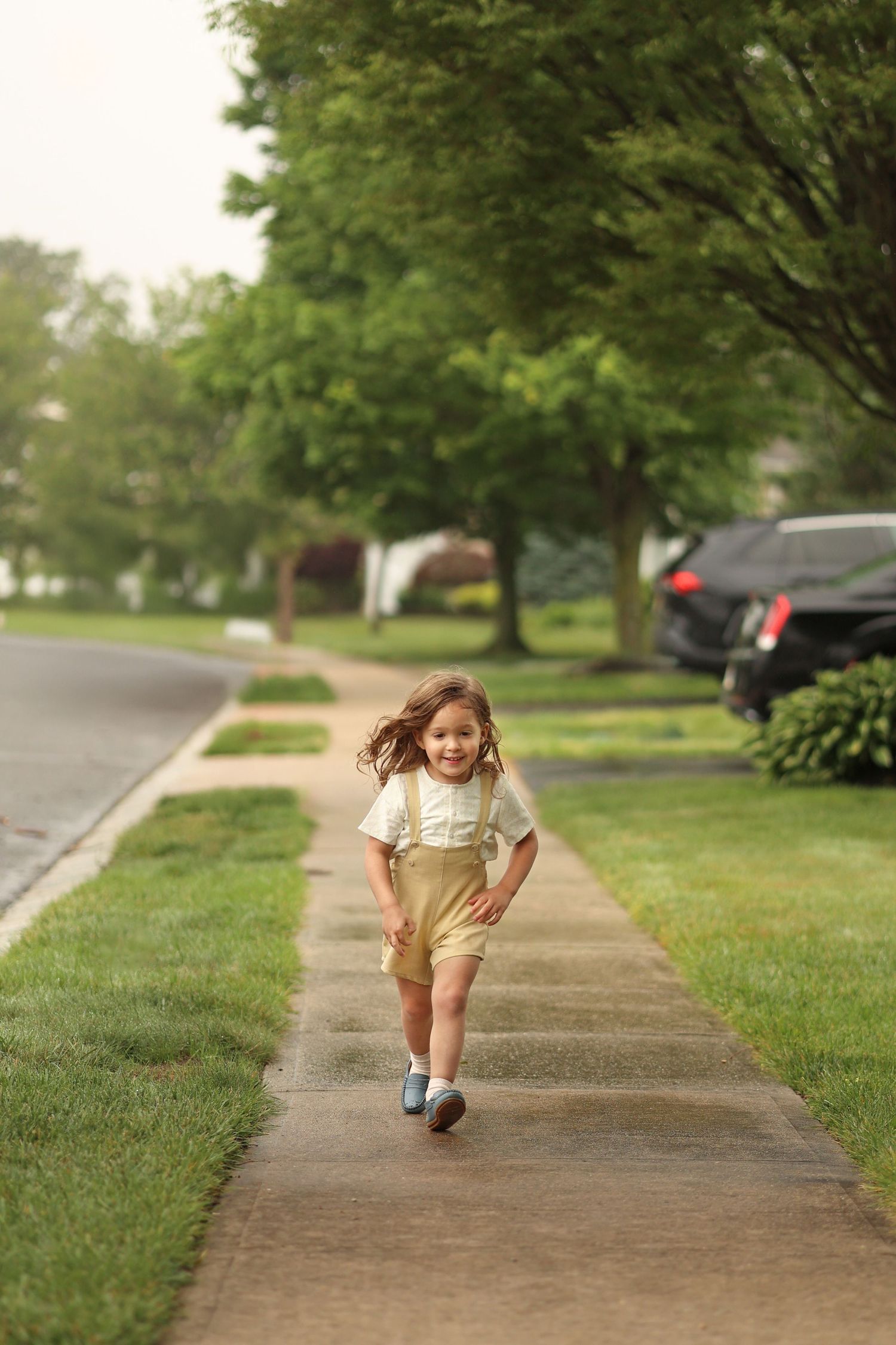 Candid lifestyle shot of a upsherin boy running down a suburban sidewalk towards the camera