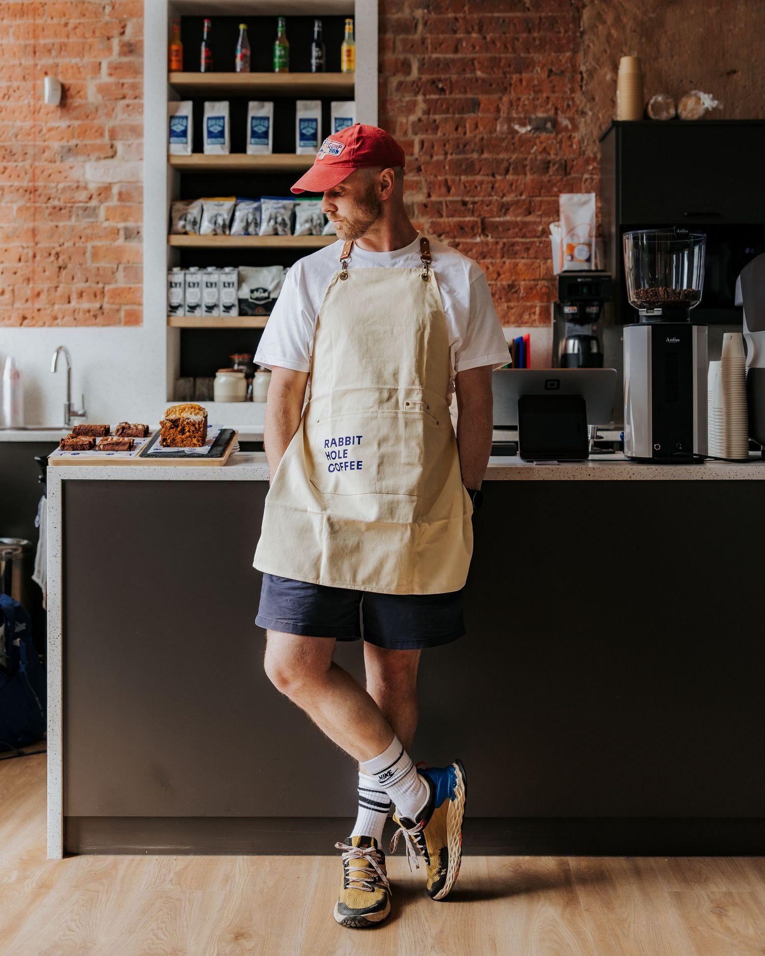 Coffee shop interior with exposed brick walls, wooden counter, and staff members in white aprons working behind the bar.