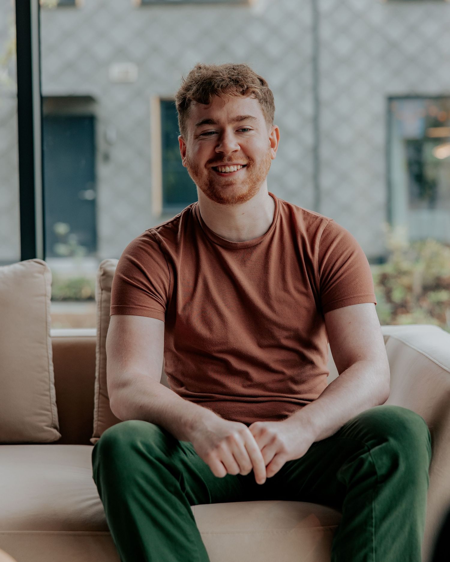 Person in a brown t-shirt and green pants sitting casually on a couch in a modern interior setting.